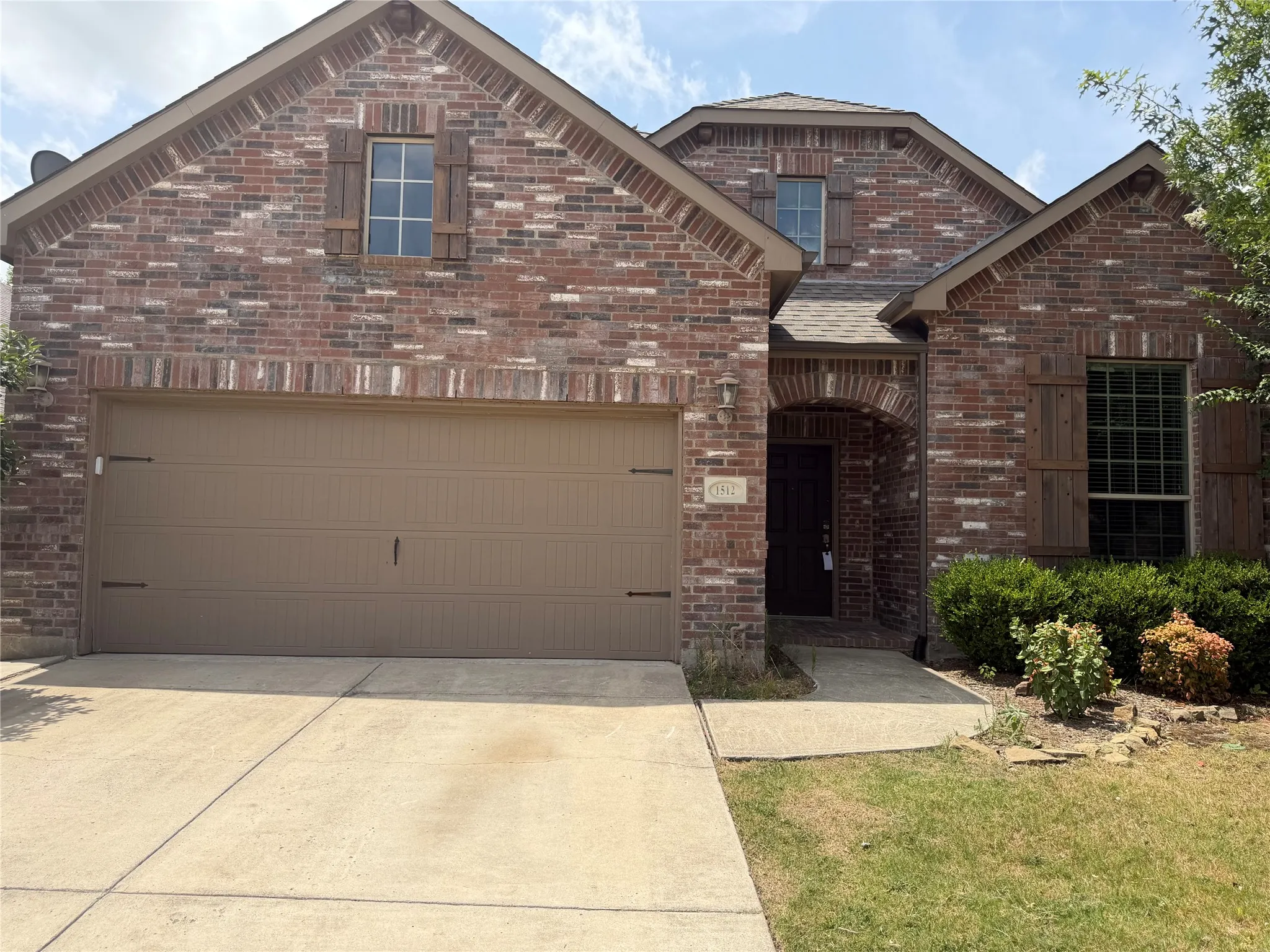 Brick exterior featuring a two-car garage, arched entry, and decorative shutters