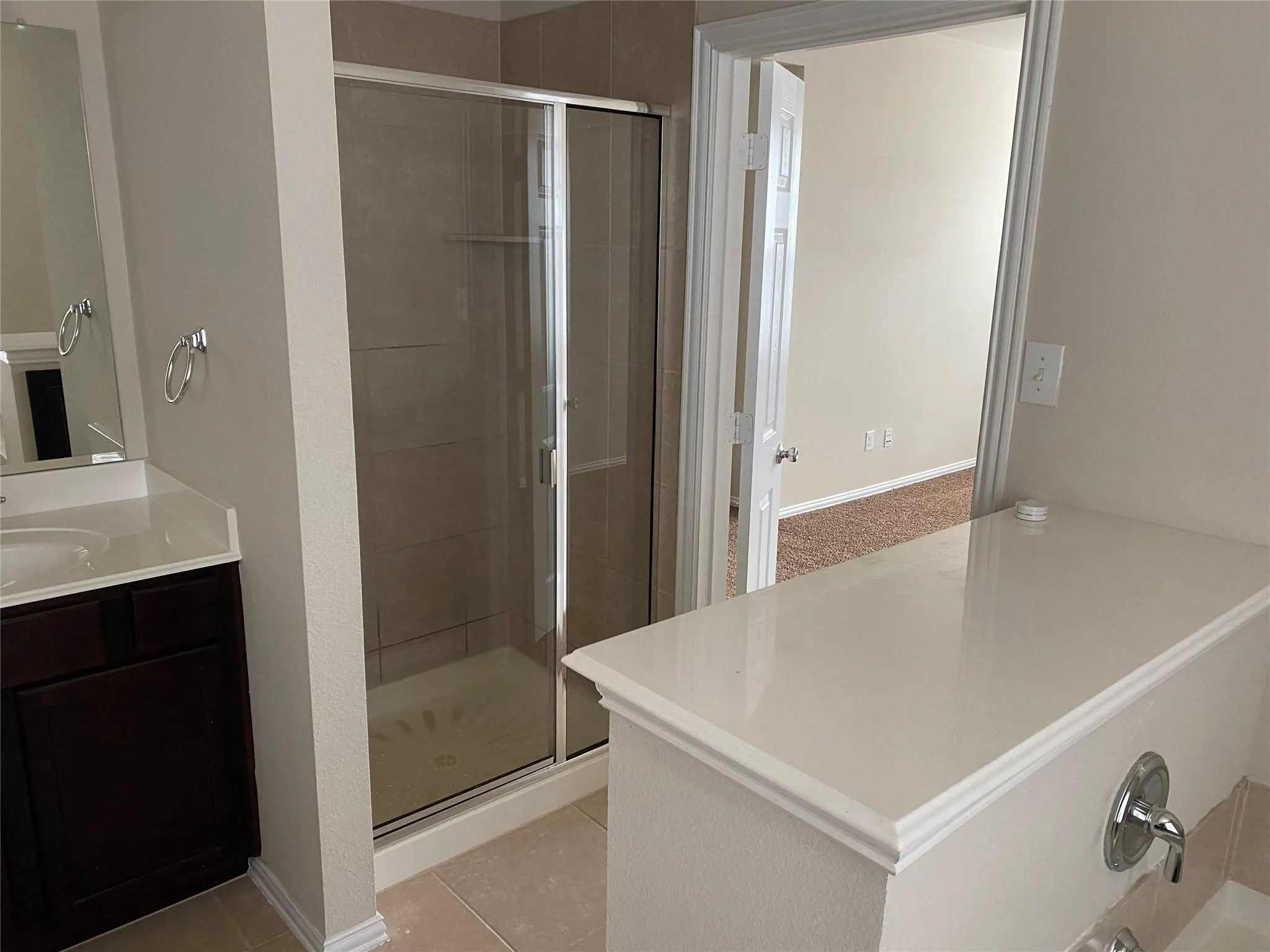 Bathroom featuring a glass-enclosed shower with tile surround, a dark wood-finish vanity with an integrated sink and light-toned countertop, and tile flooring