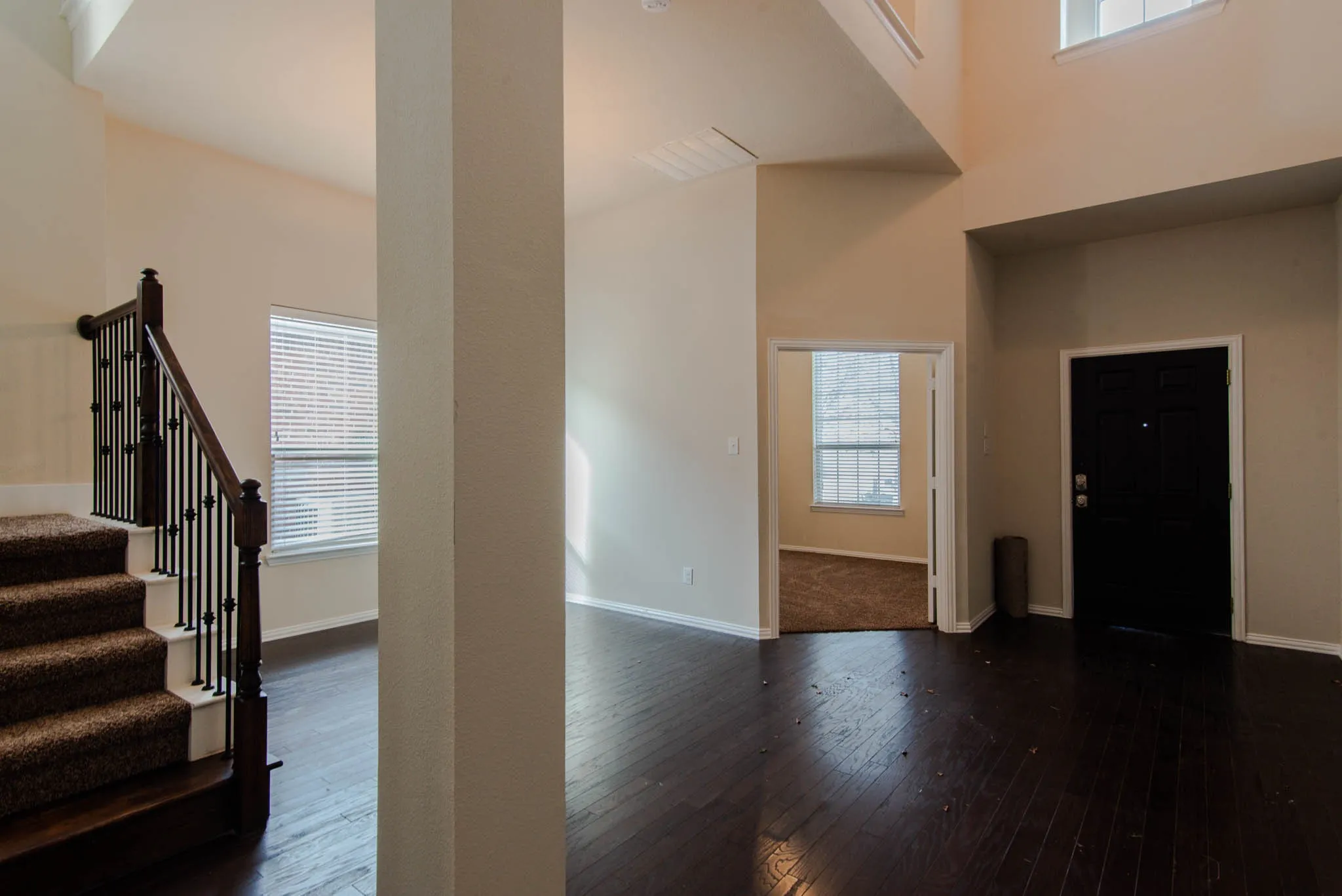 Grand entry featuring rich wood-finish flooring, a carpeted staircase with dark wood newel posts and iron balusters, and a soaring vaulted ceiling