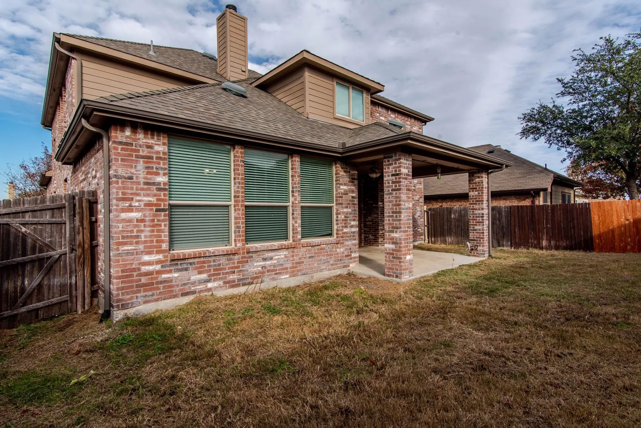 Brick exterior featuring multiple windows with blinds, a covered patio with brick columns, and a private wooden fence