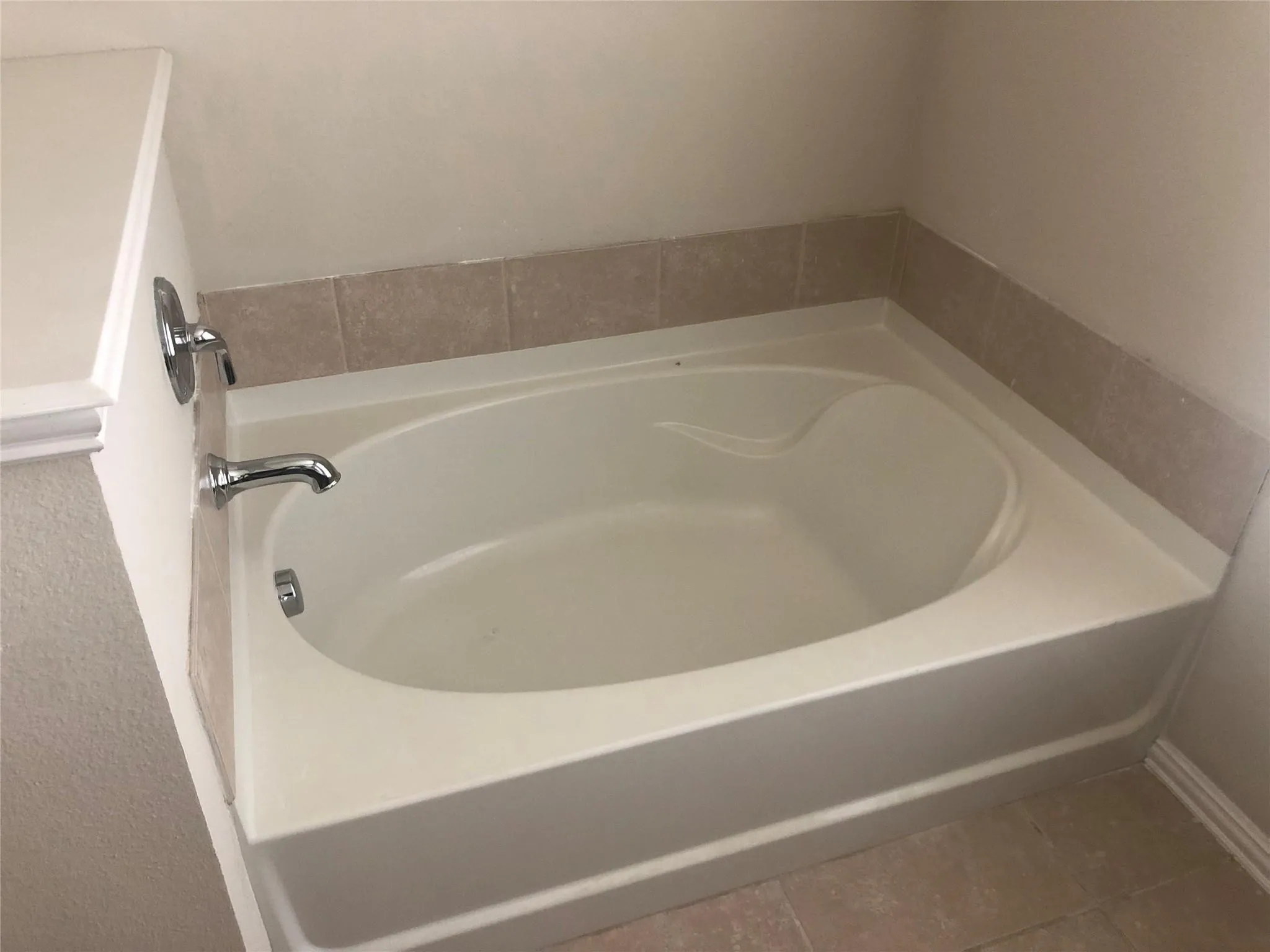 Soaking tub with integrated armrests, featuring a chrome faucet and textured wall tile surround