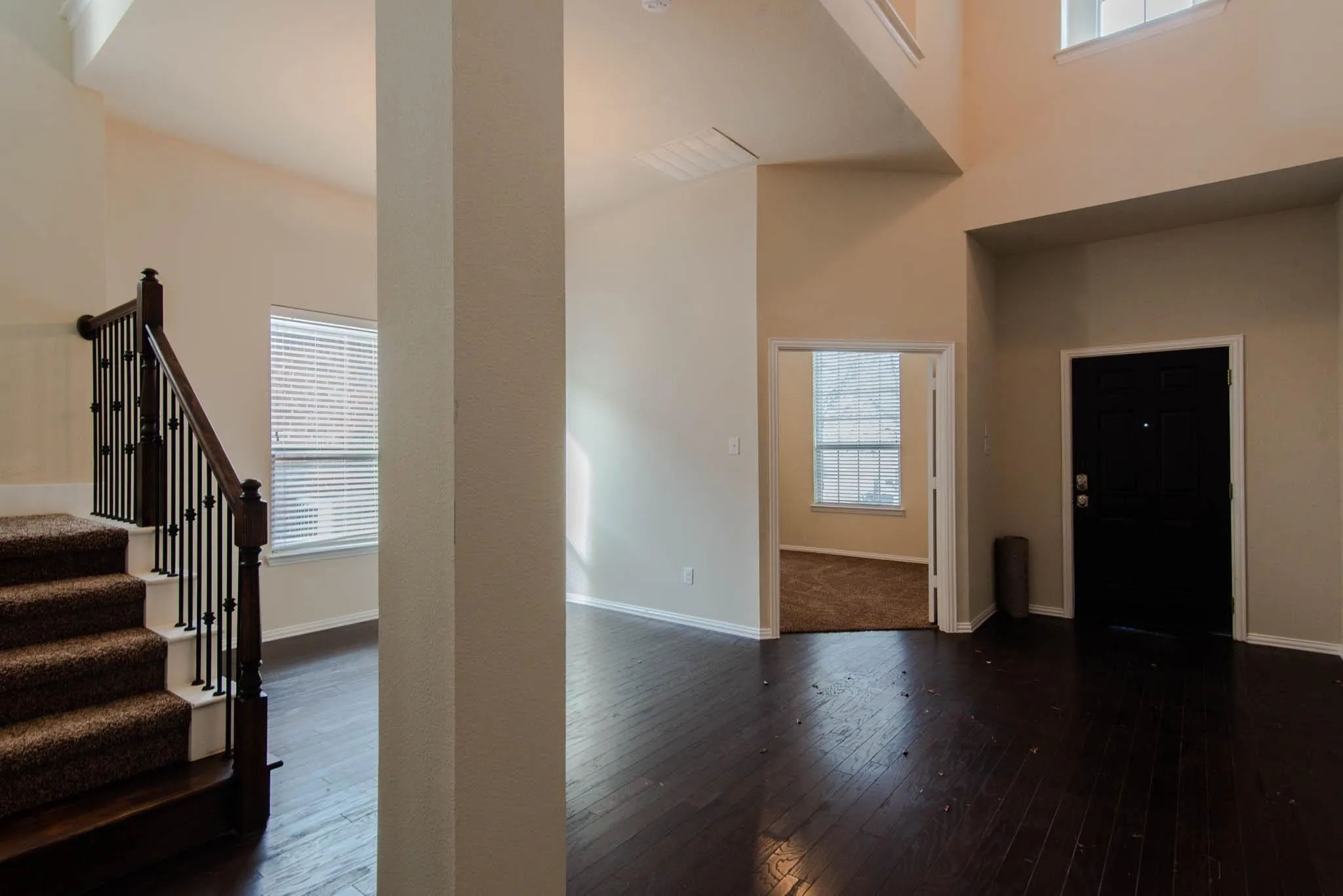 Foyer entry featuring dark wood-finish flooring, a carpeted staircase with dark wood newel posts and iron balusters, and a black paneled front door