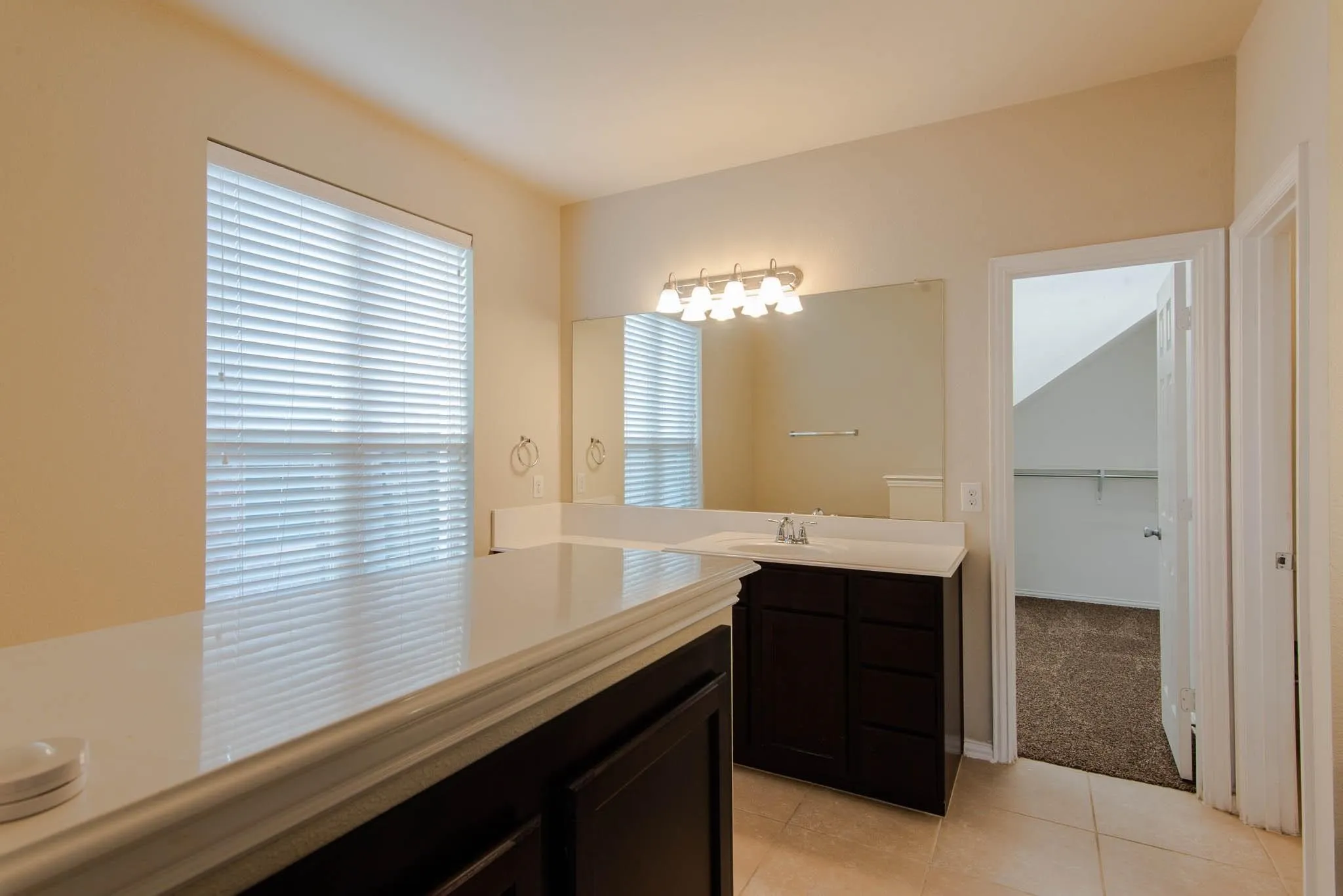 Bathroom featuring dual dark wood vanities with white countertops, a large wall-mounted mirror, and tile flooring