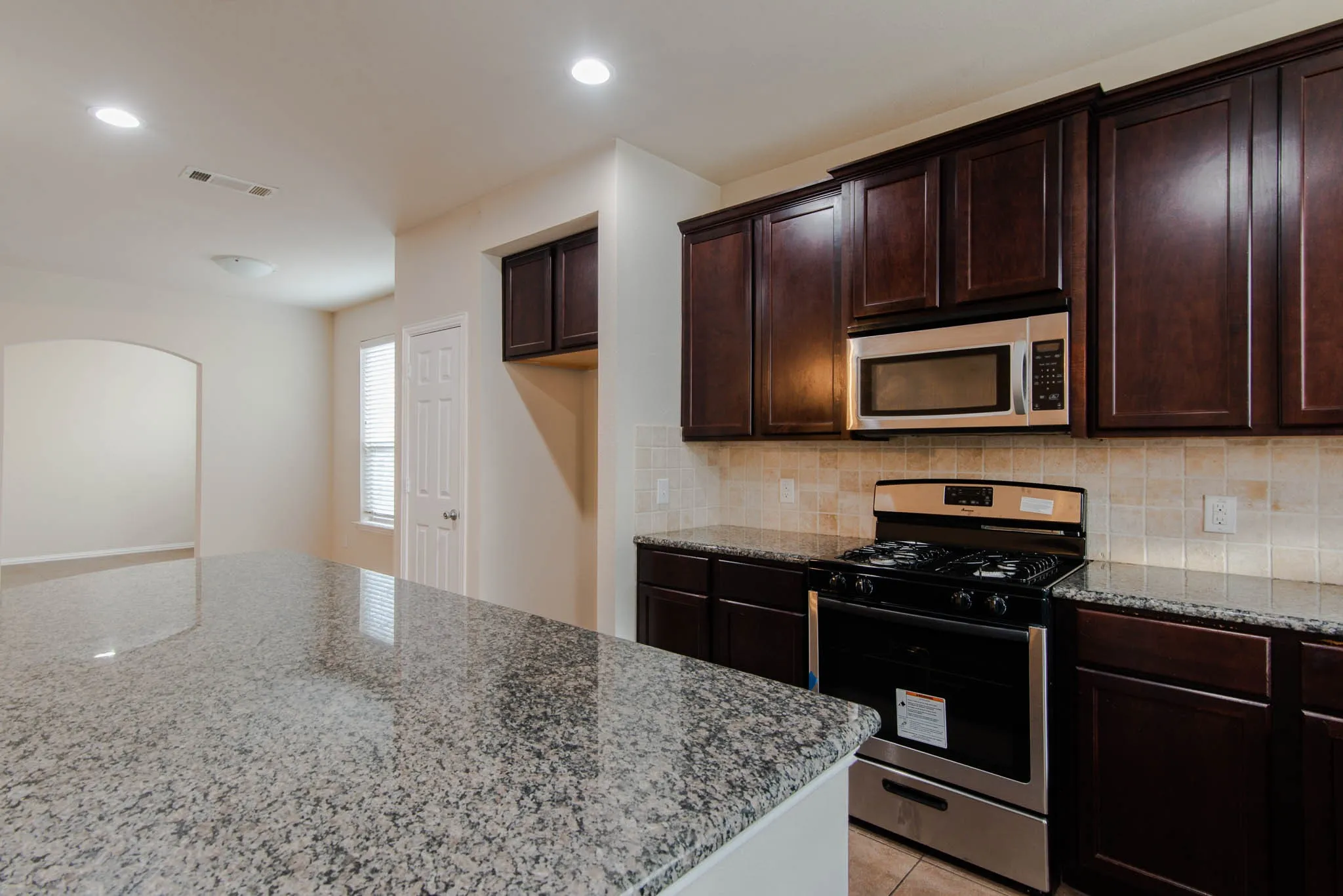 Kitchen featuring an expansive granite island, dark wood-finish cabinetry, stainless steel appliances, and tile flooring