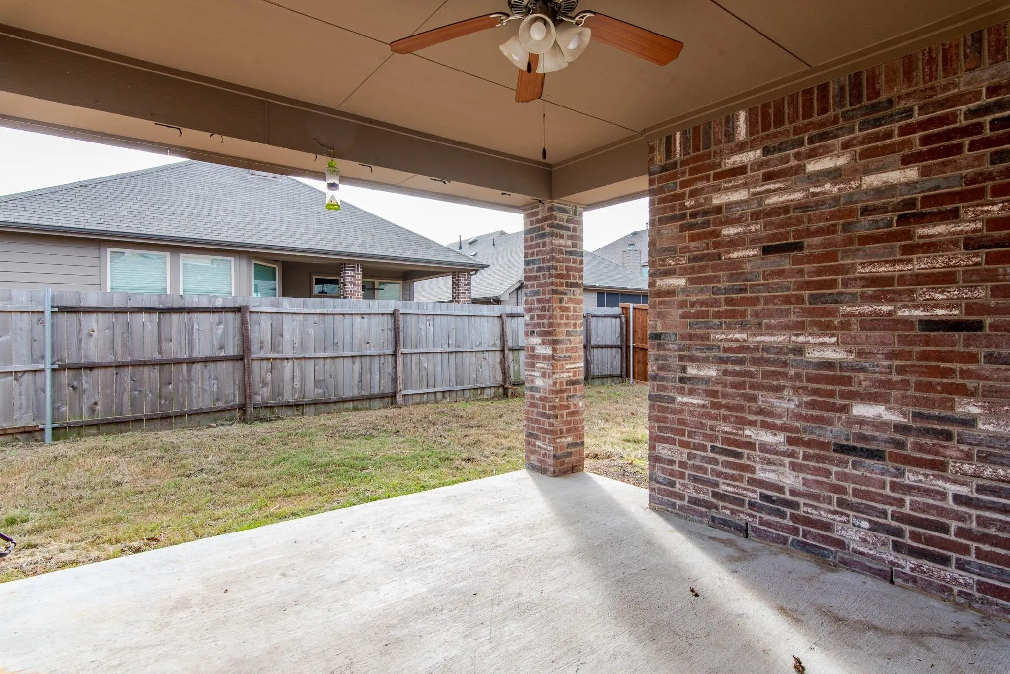 Covered patio featuring a ceiling fan, concrete flooring, and a multi-tone brick exterior wall and column
