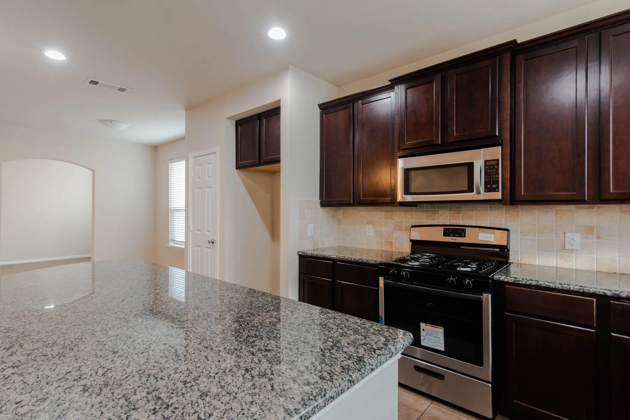 Kitchen featuring dark wood-finish cabinetry, stainless steel appliances, speckled stone countertops, and a tile backsplash