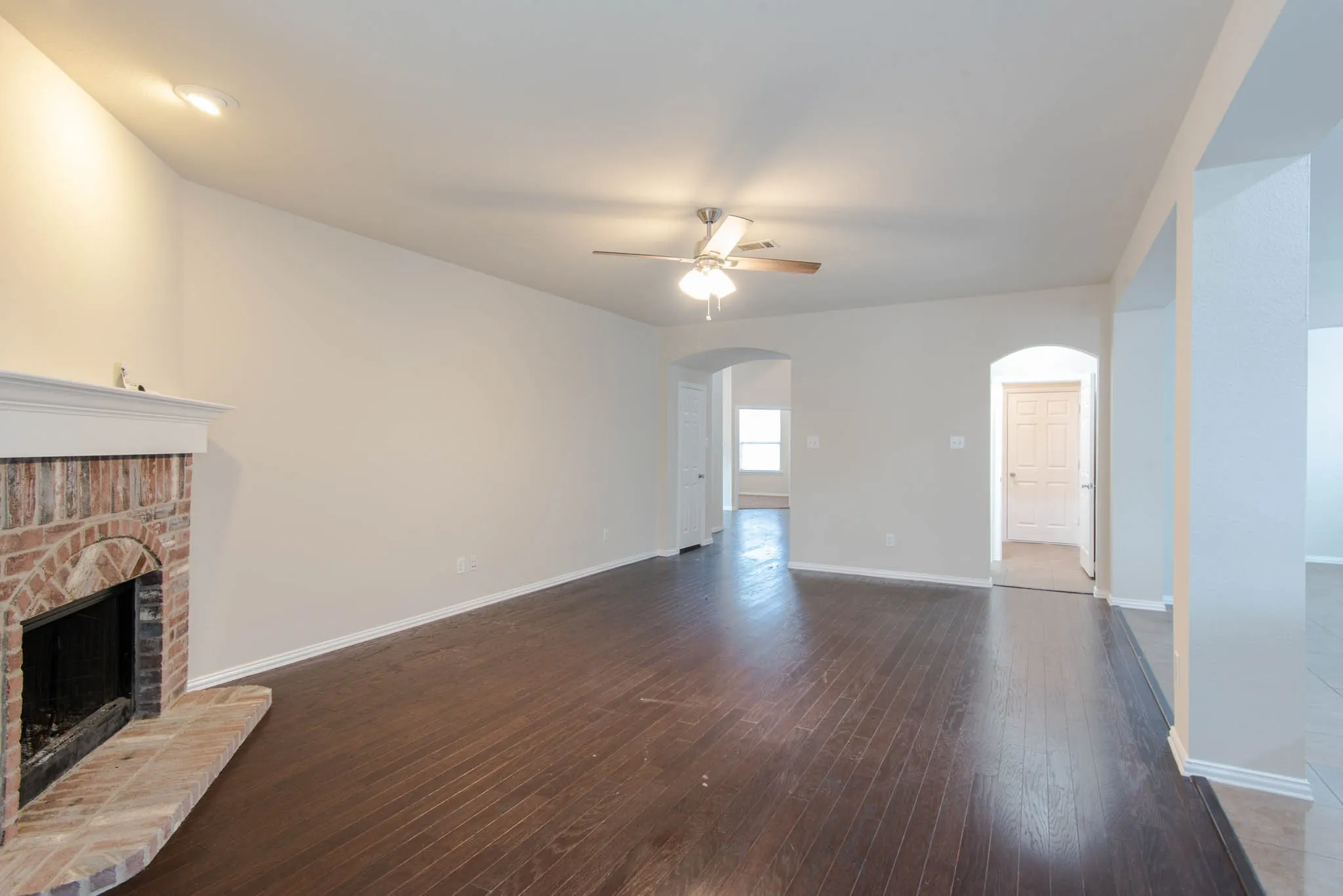 Spacious living area featuring wood-finish flooring, a brick fireplace with a white mantle, vaulted ceilings, and recessed lighting