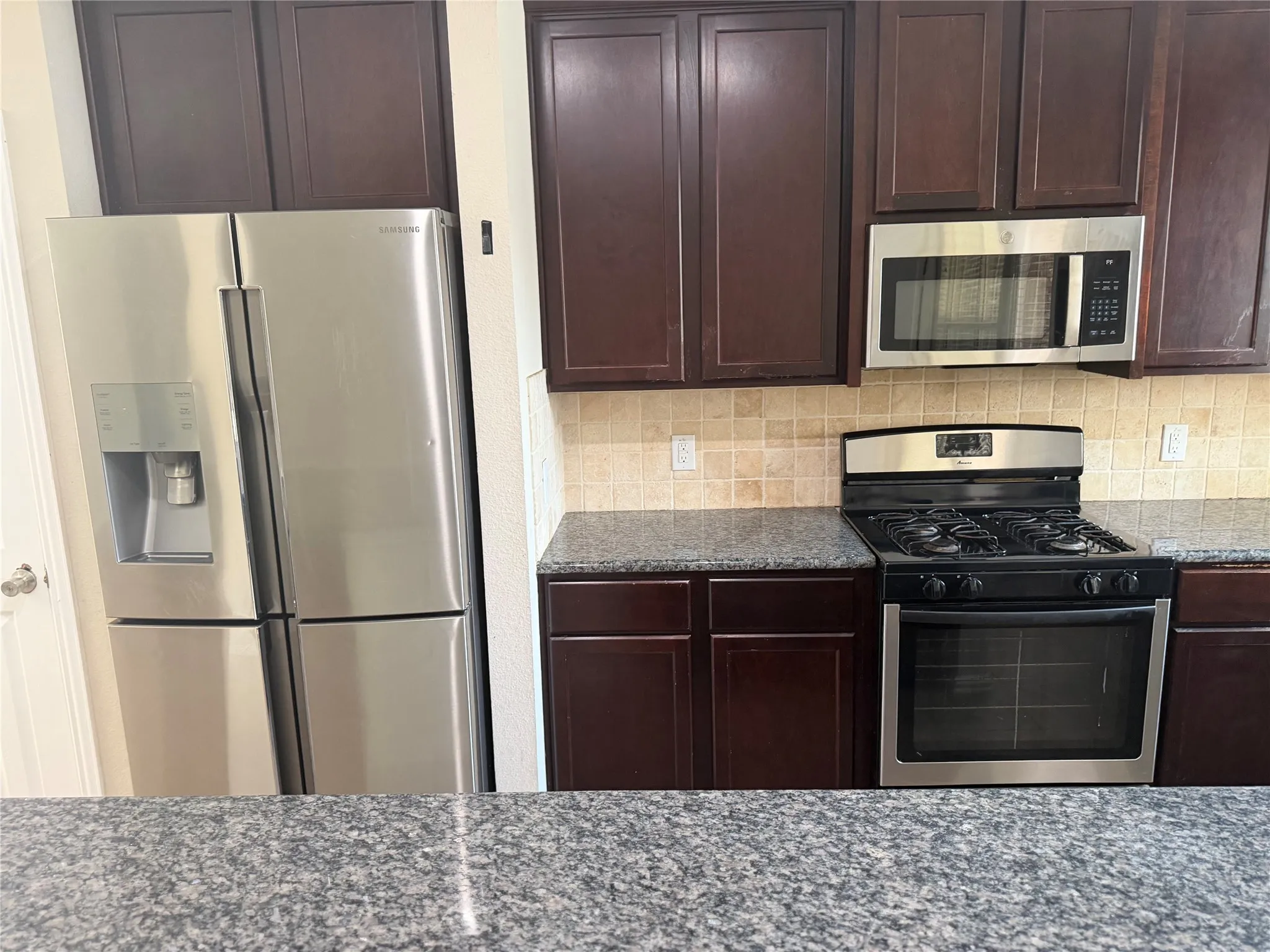 Kitchen featuring dark wood cabinetry, granite-style countertops, and a tiled backsplash