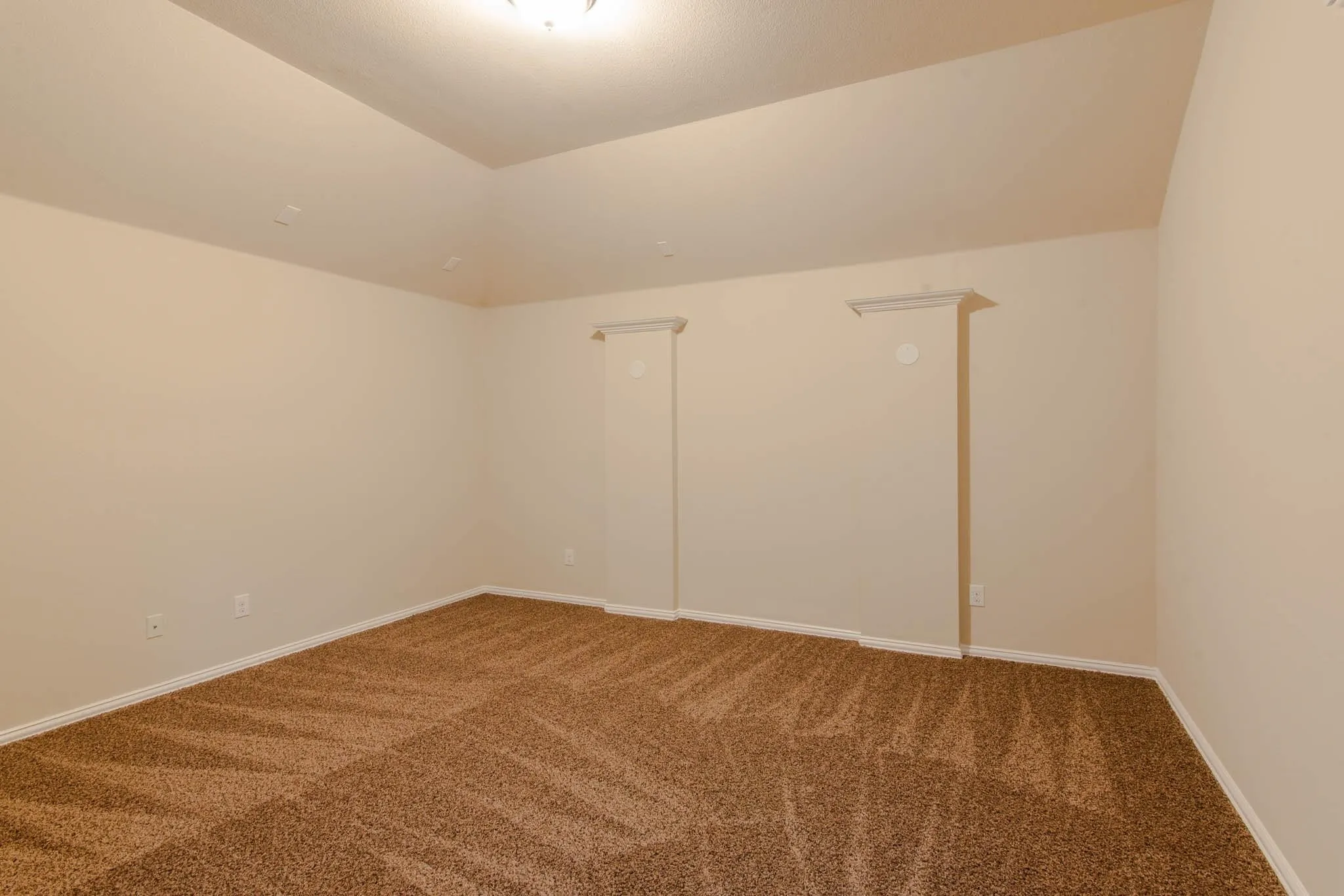 Spacious room featuring vaulted ceilings, light-colored walls, brown patterned carpeting, white baseboards, and ceiling-mounted lighting