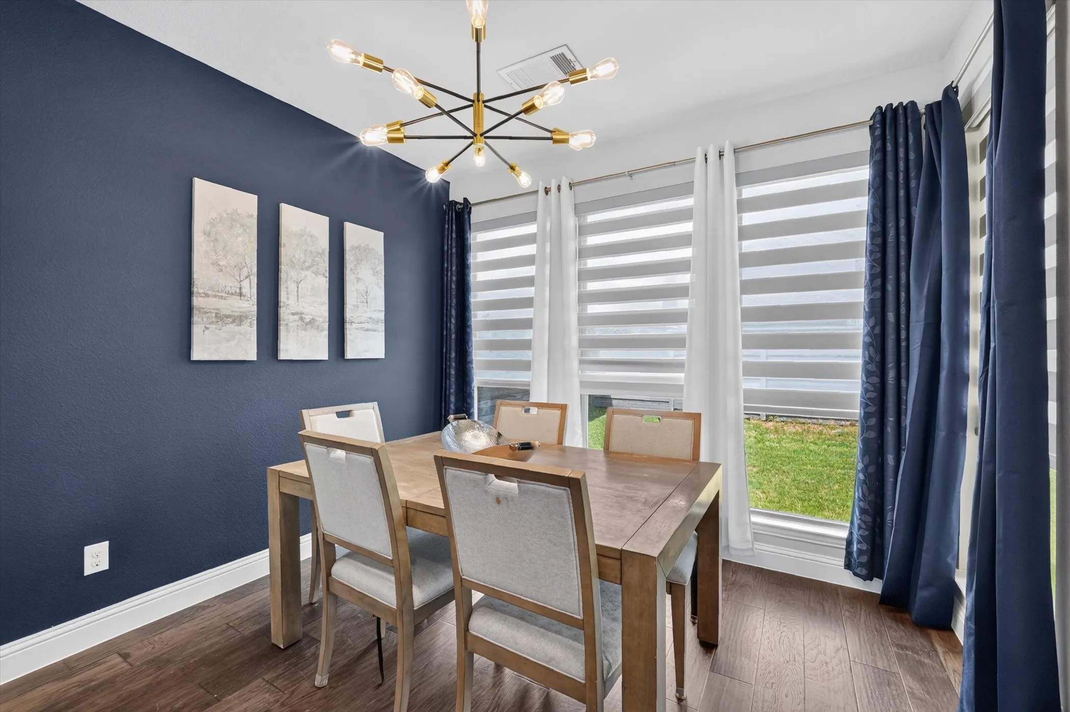 Dining space featuring a linear chandelier, rich wood-finish flooring, and a deep blue accent wall