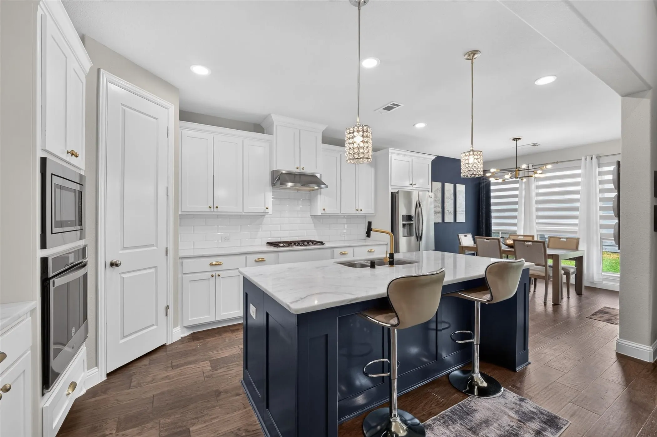 Kitchen featuring a large central island with seating, white shaker-style cabinetry, built-in stainless steel appliances, a subway tile backsplash, and wood-finish flooring