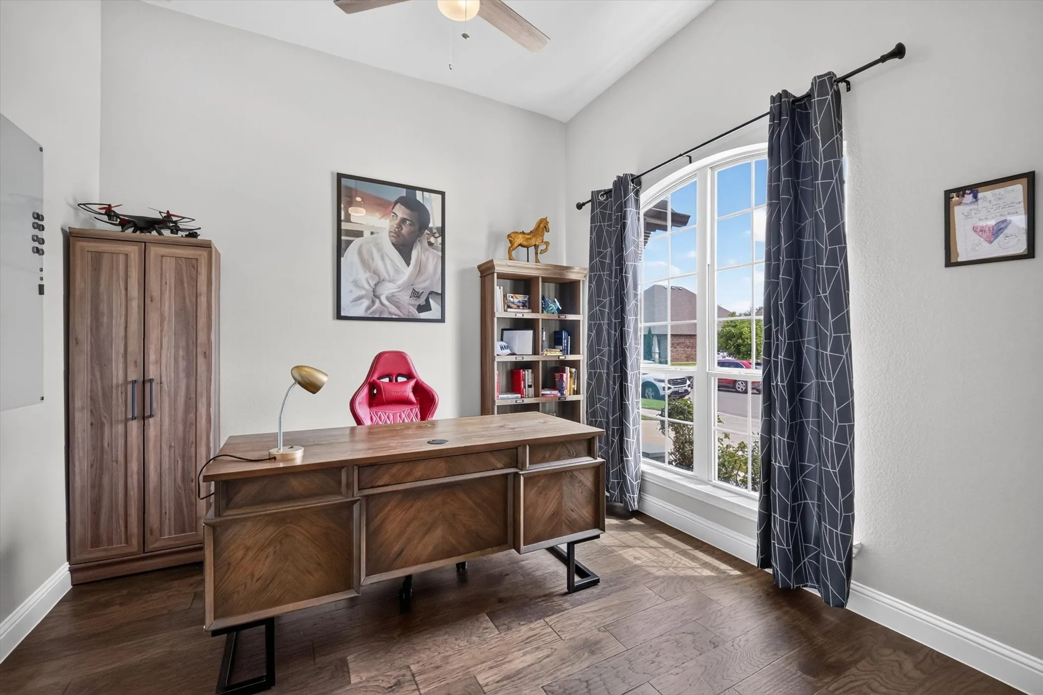 High vaulted ceiling room with wood-finish flooring, a large arched window, and a ceiling fan
