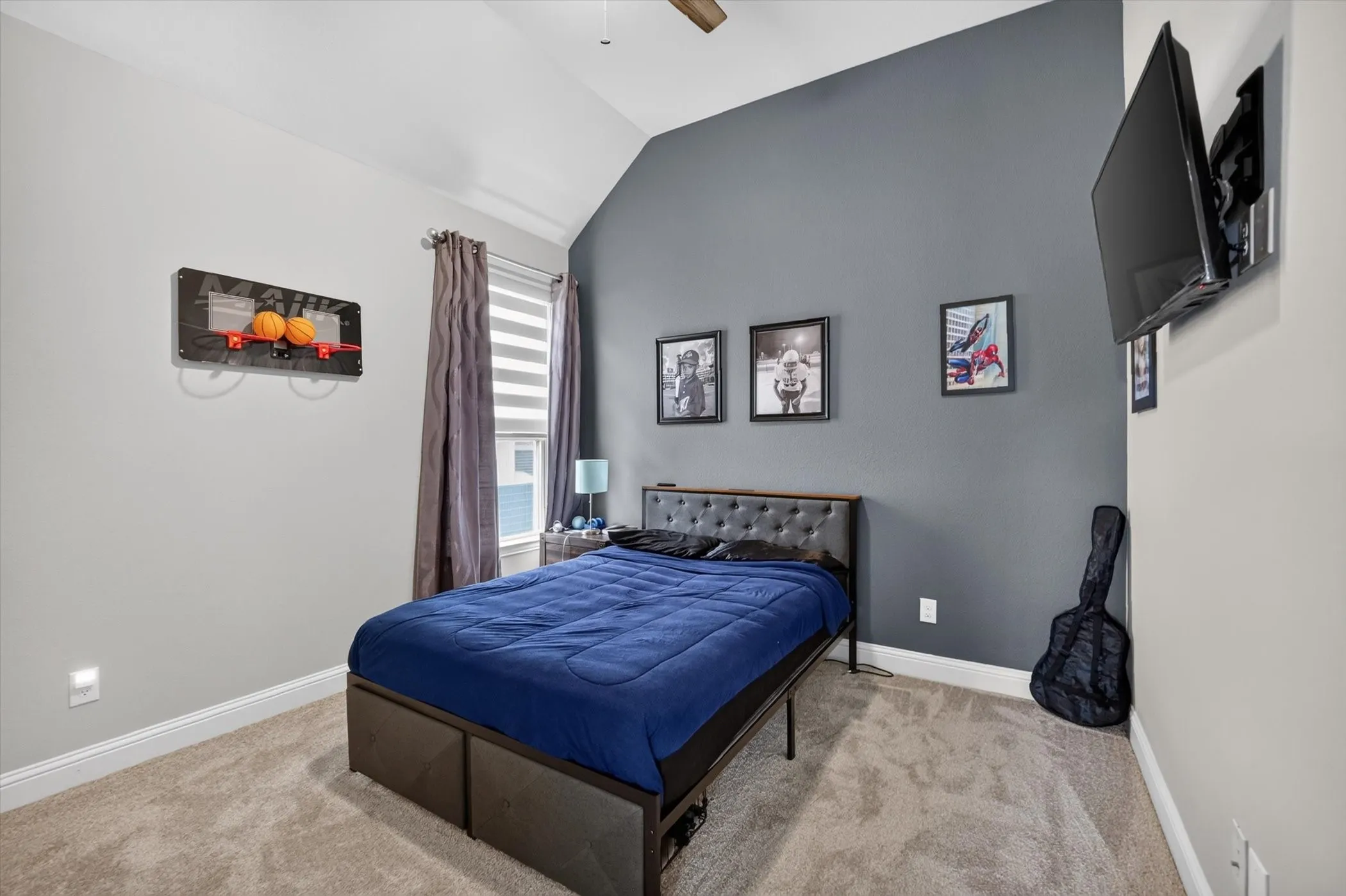Vaulted ceiling bedroom featuring a window with blinds and drapes, wall-mounted television, and neutral tone carpet