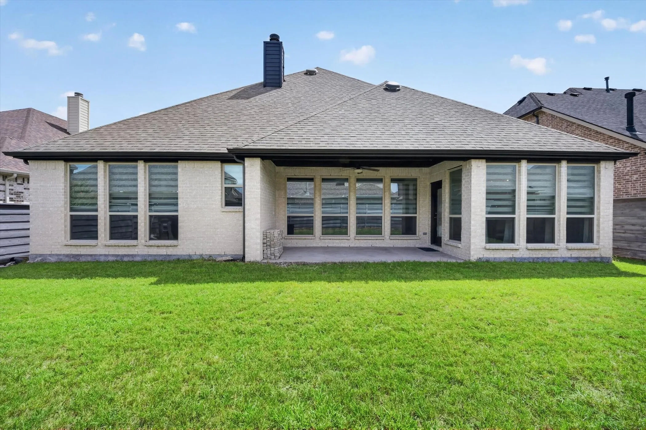 Expansive rear facade featuring light brick masonry, a covered patio, and a shingled roof