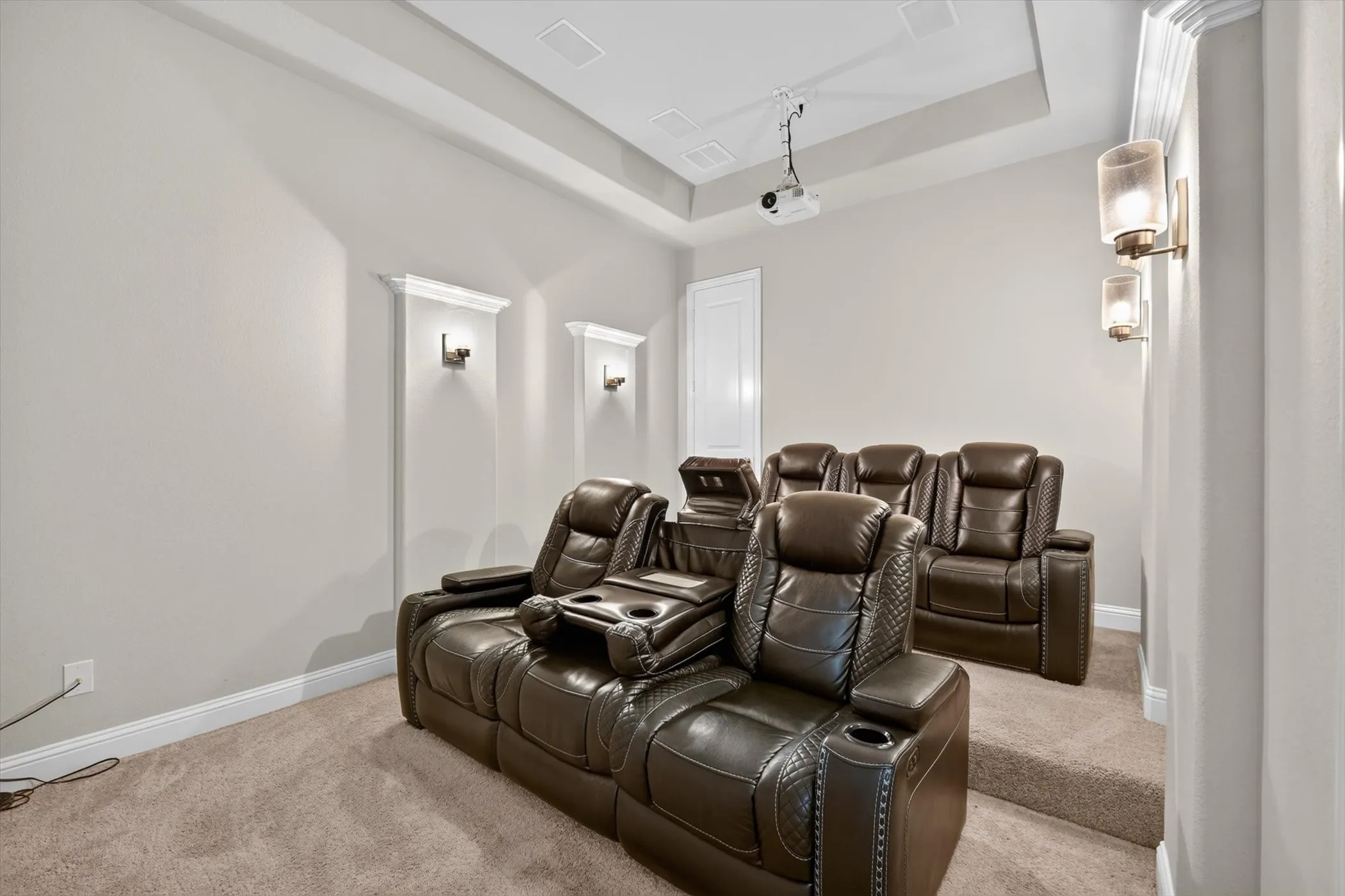 Dedicated media room featuring tray ceiling, recessed speakers, sconce lighting, and layered carpeted flooring