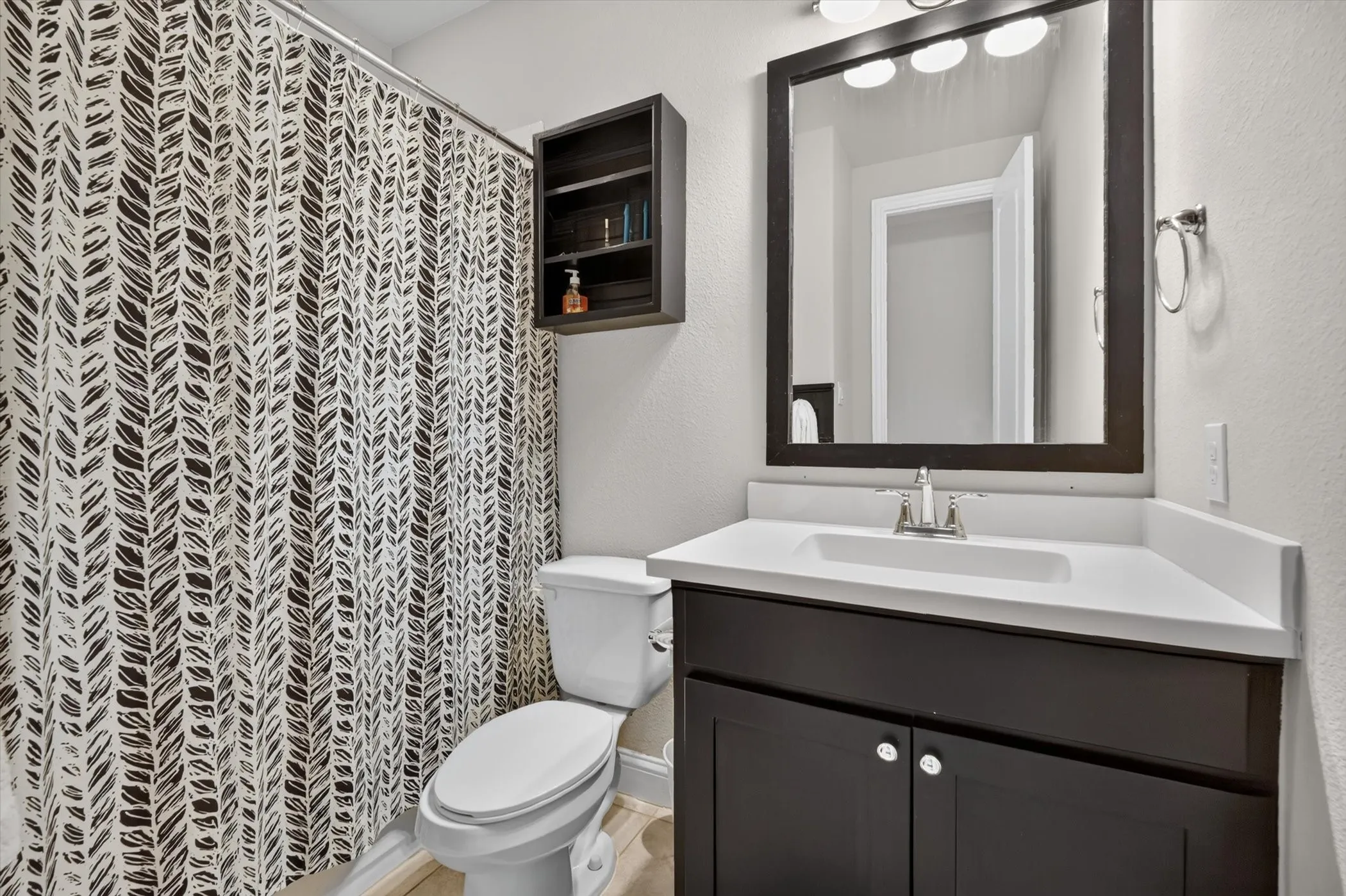 Bathroom featuring a dark wood-finish vanity with a white countertop and integrated sink, framed mirror, and three-bulb vanity lighting