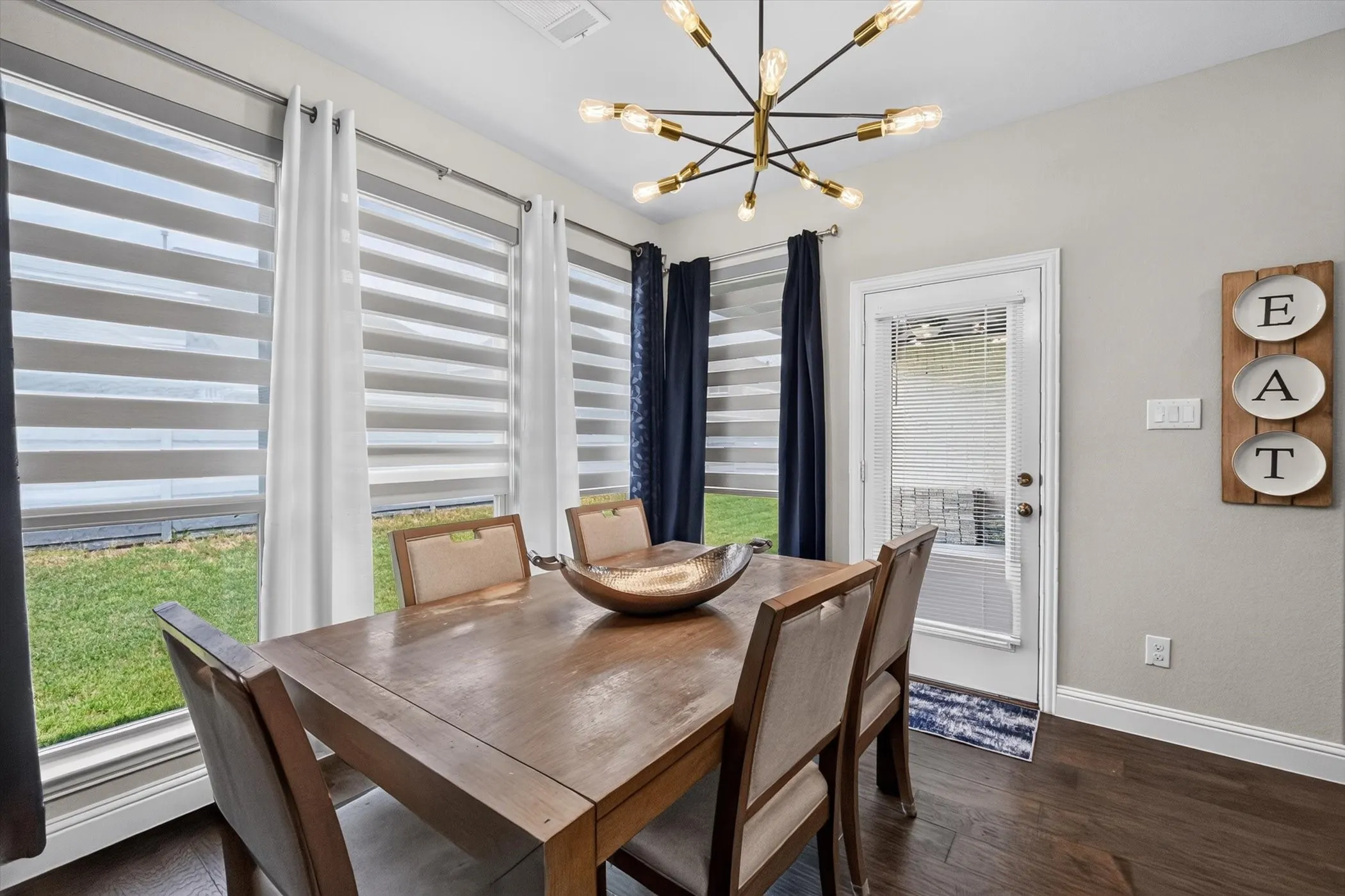 Dining area featuring a contemporary sputnik chandelier, dark wood-finish flooring, and multiple windows with layered blinds and drapery