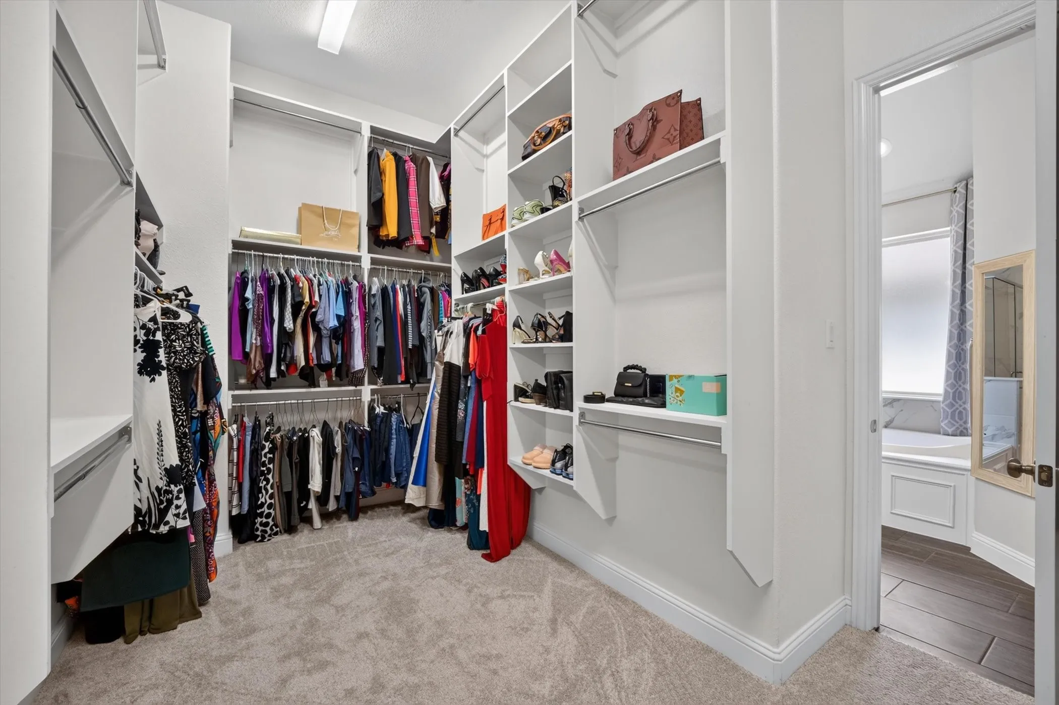 Expansive walk-in closet featuring extensive built-in shelving, multiple hanging rods, and light-colored carpeting