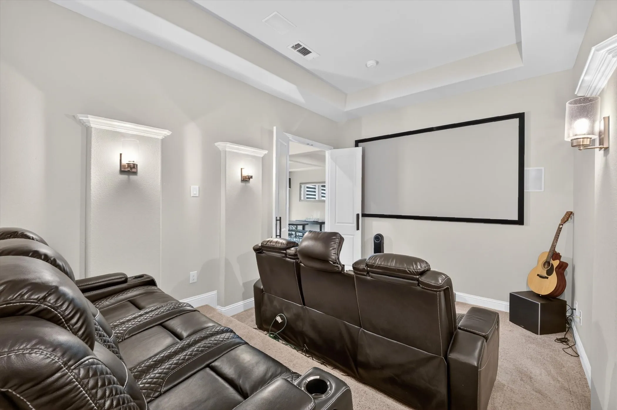 Dedicated media room featuring a large projection screen, recessed ceiling lighting, and built-in wall sconces