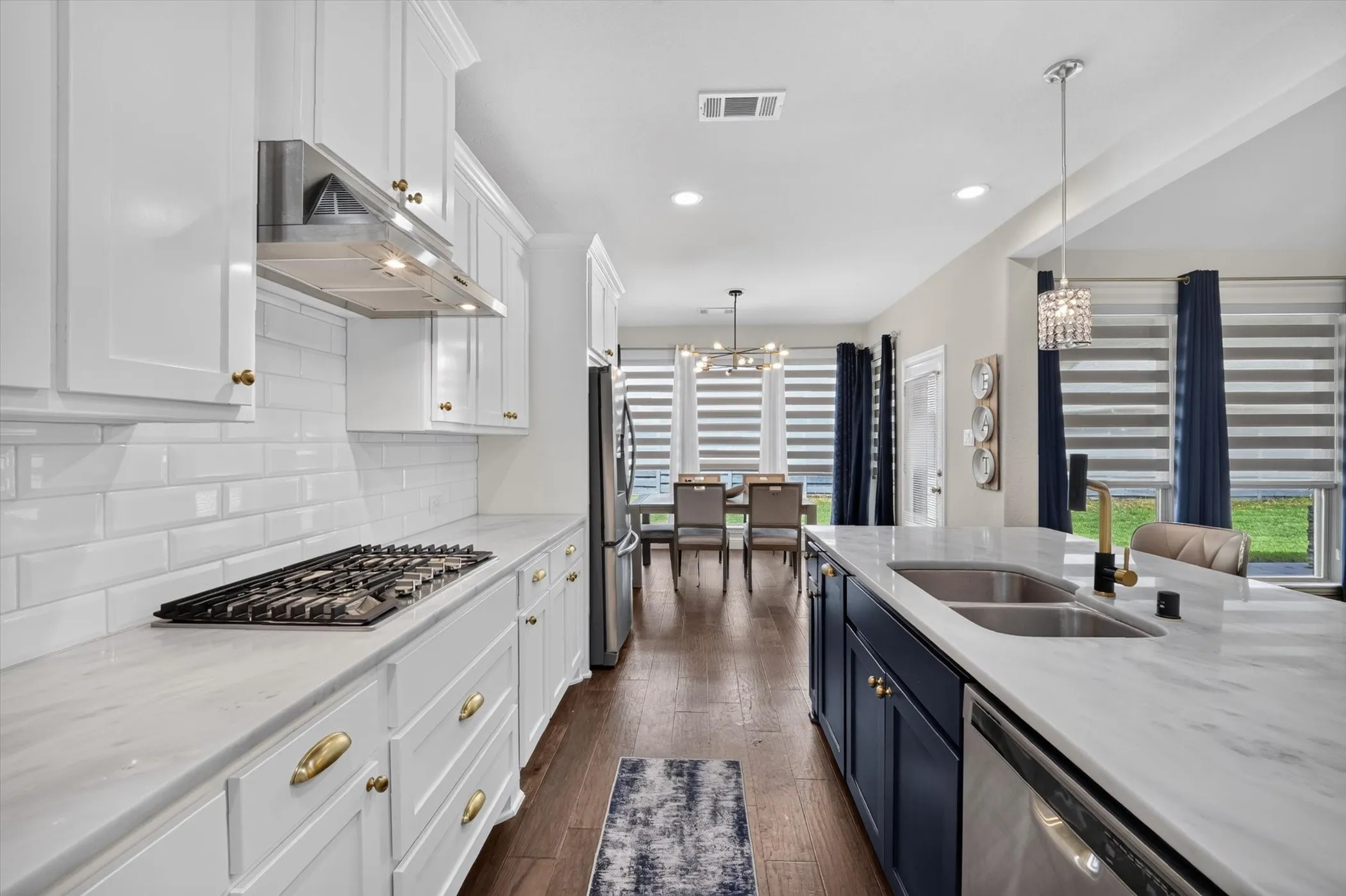 Gourmet kitchen featuring a gas cooktop, stainless steel range hood, subway tile backsplash, and white cabinetry with brass hardware