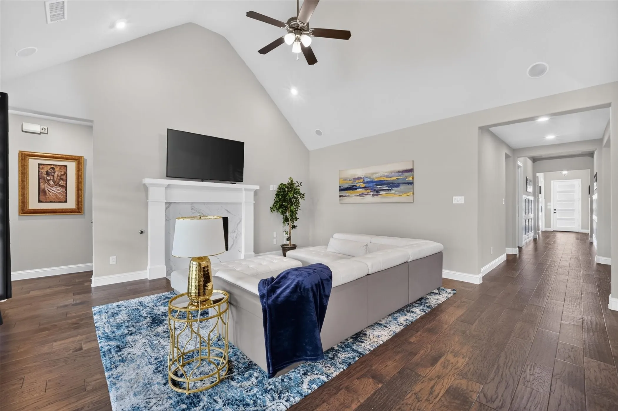 Spacious living area featuring a vaulted ceiling with a ceiling fan, a fireplace with a white mantel and marble surround, recessed lighting, and wood-finish flooring