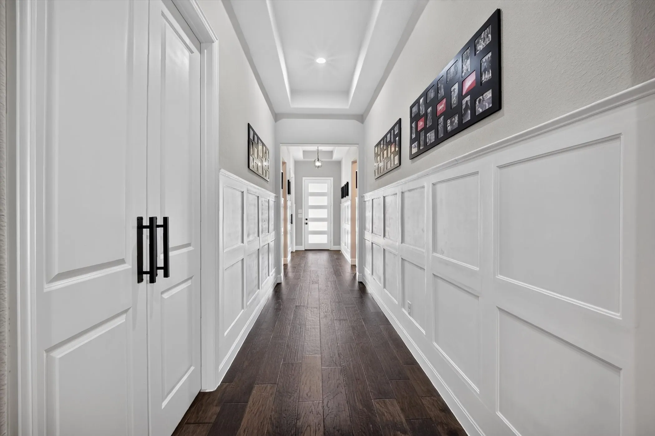 Hallway featuring dark wood-finish flooring, white wainscoting, white doors with modern black hardware, and a tray ceiling