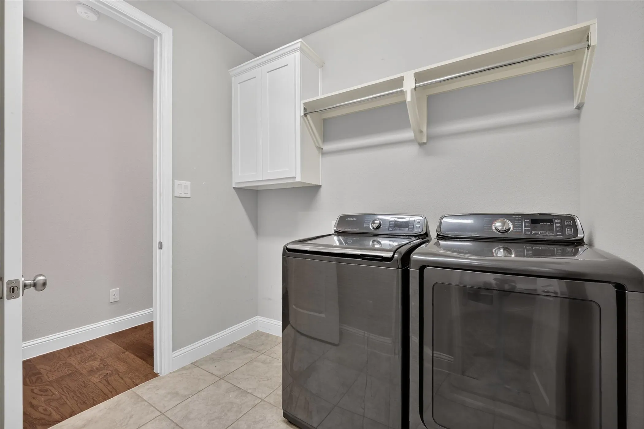 Utility space featuring light gray walls, tile flooring, white baseboards, and a white upper cabinet