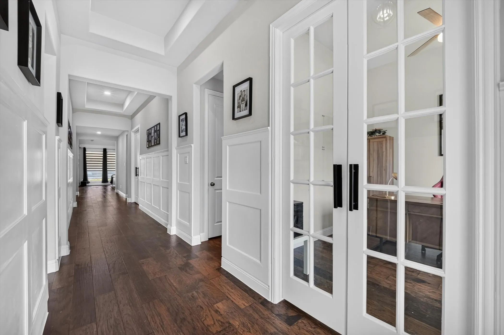 Hallway featuring wood-finish flooring, wainscoting, coffered ceiling details, recessed lighting, and French doors with black hardware