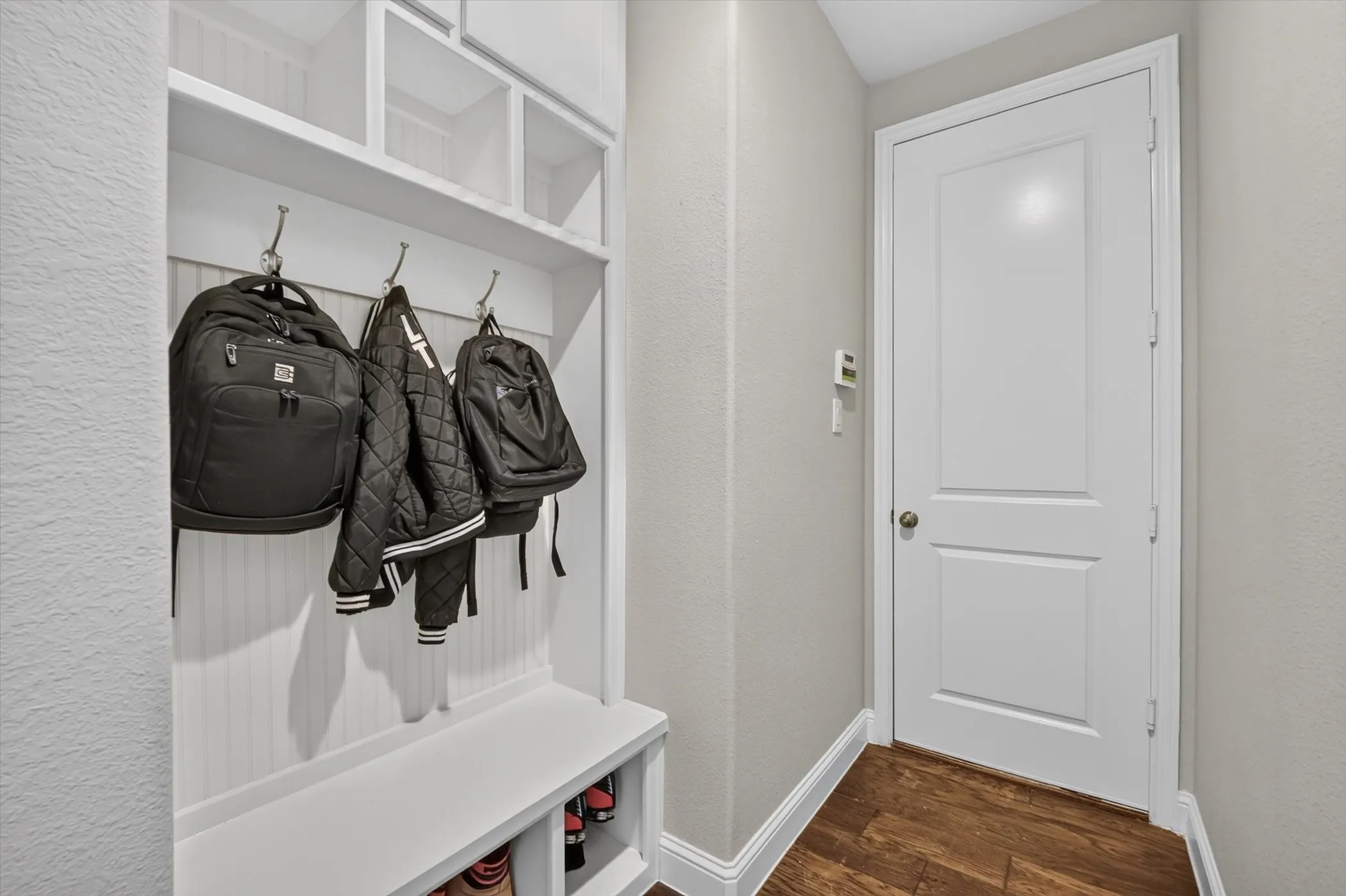 Built-in mudroom bench with coat hooks and overhead cubby storage, featuring wood-finish flooring and a two-panel interior door