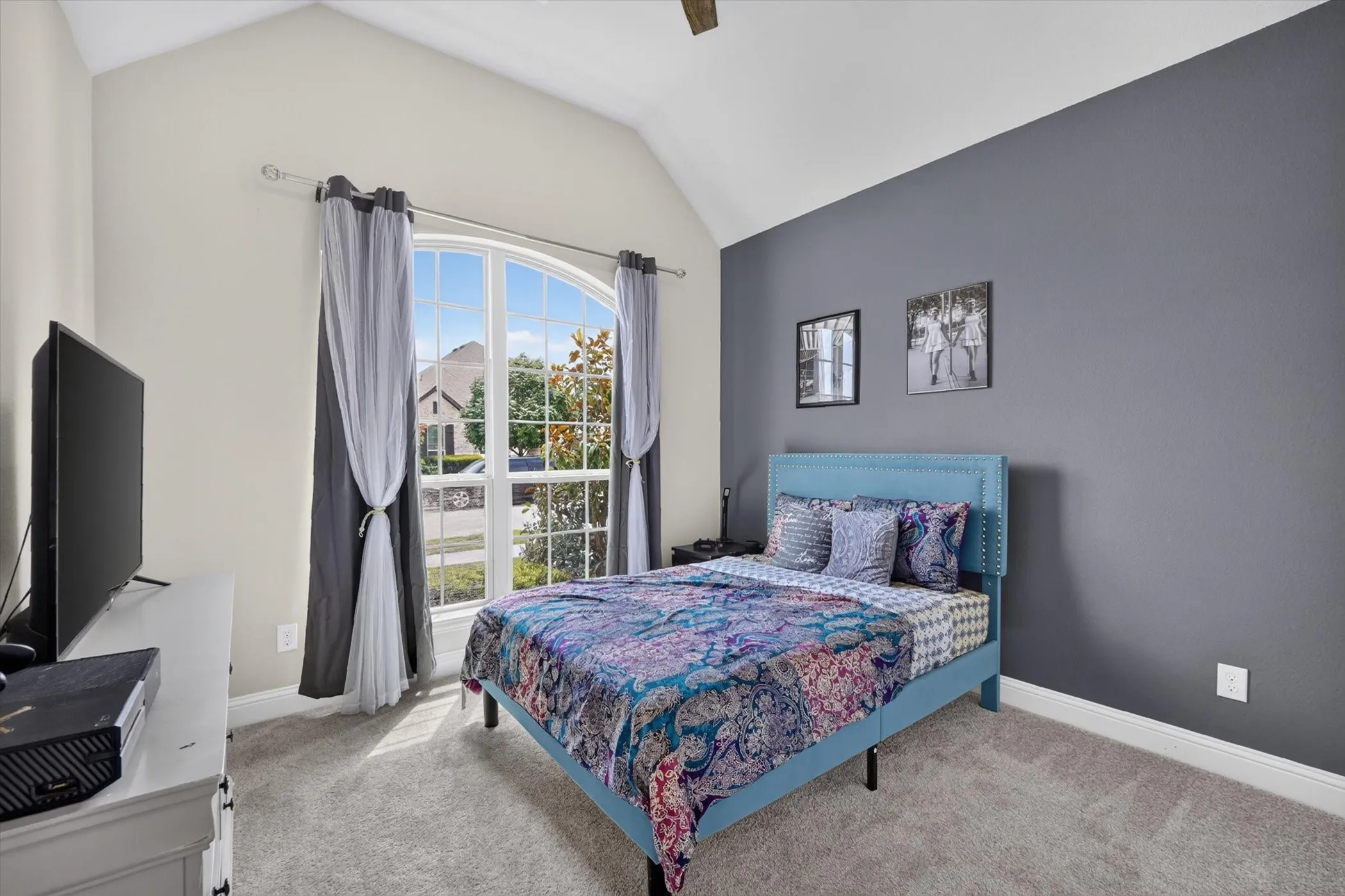 Vaulted ceiling room featuring an arched window, light gray carpeting, and a contrasting accent wall