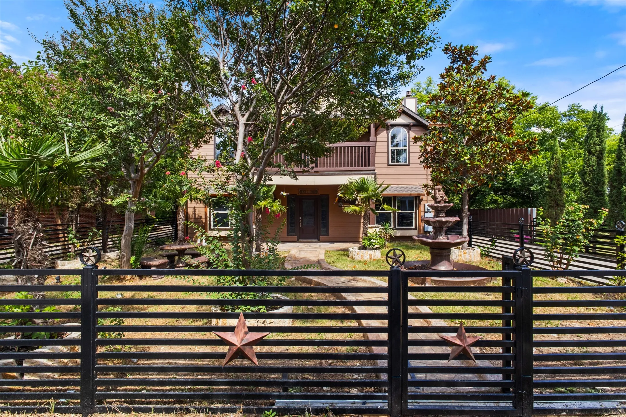 Two-story property featuring a front-facing balcony, exterior wood siding, and mature trees