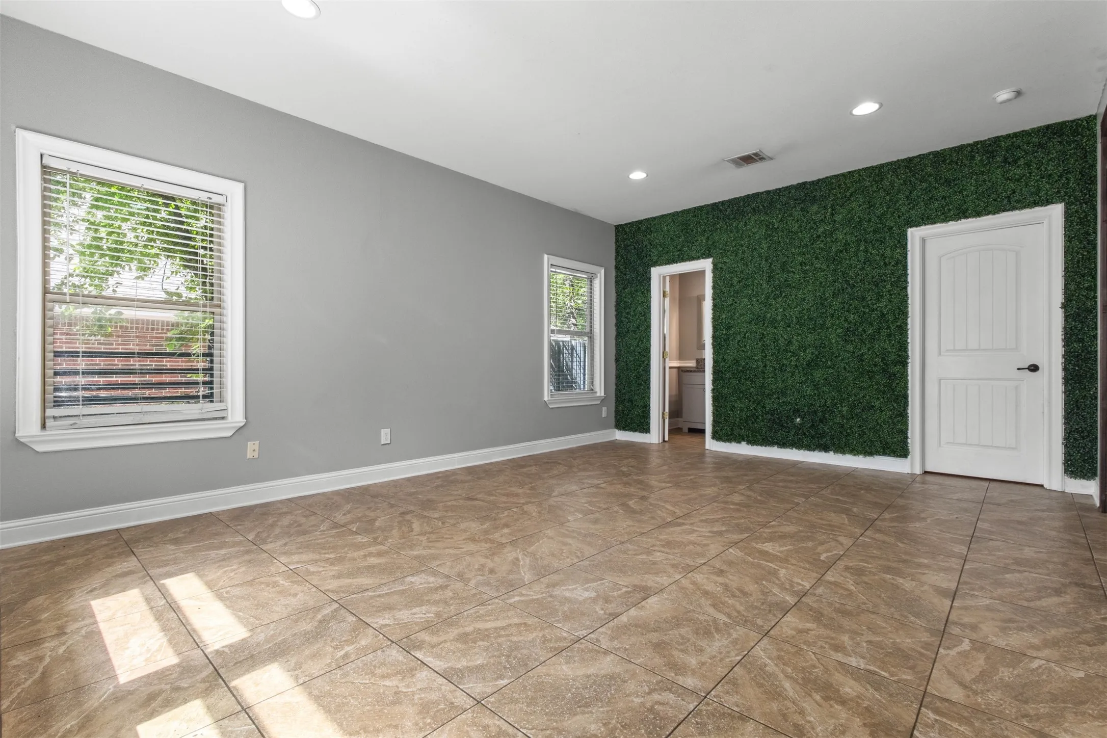 Spacious room featuring a distinctive green accent wall, neutral-toned tile flooring, recessed lighting, and white baseboards