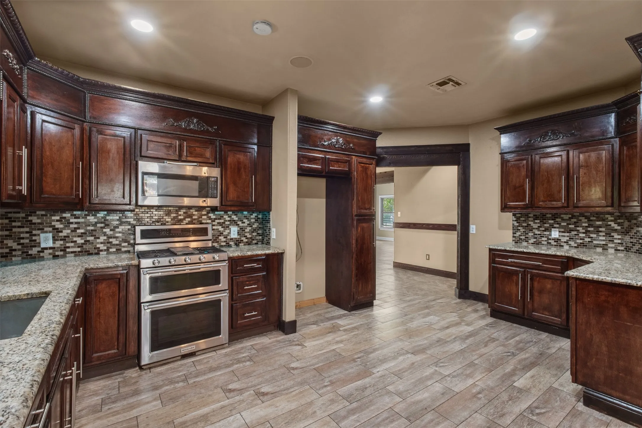 Kitchen featuring dark wood cabinetry with decorative molding, stainless steel appliances, granite countertops, and a mosaic tile backsplash