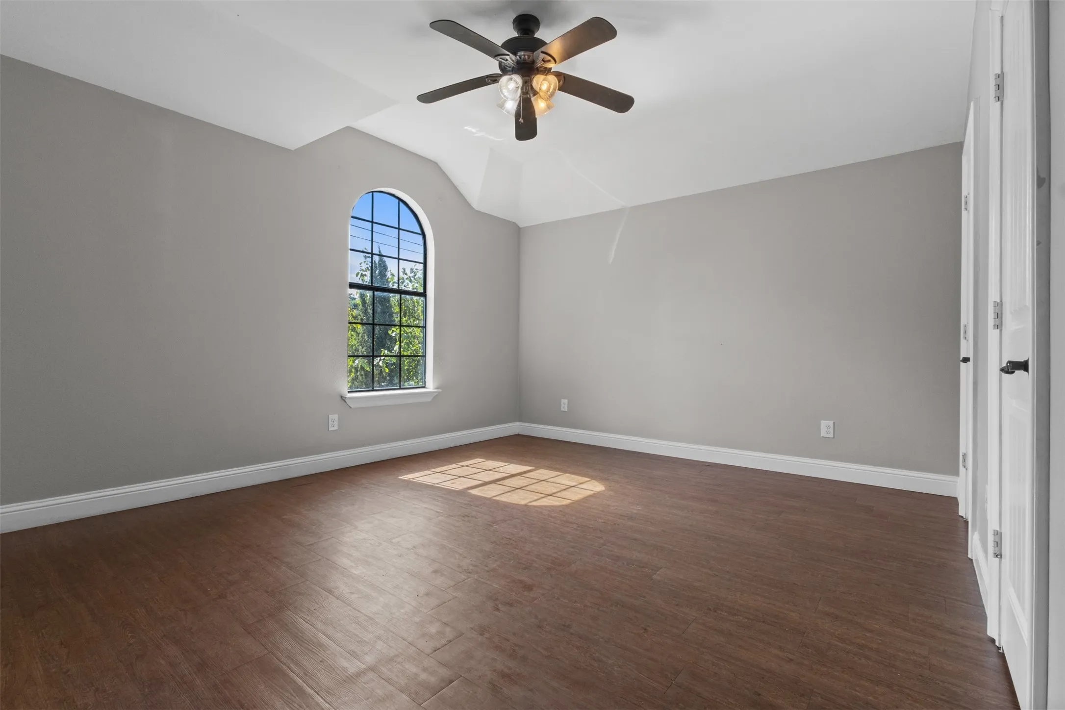 Room featuring an arched window, wood-finish flooring, a ceiling fan with integrated lighting, and a vaulted ceiling