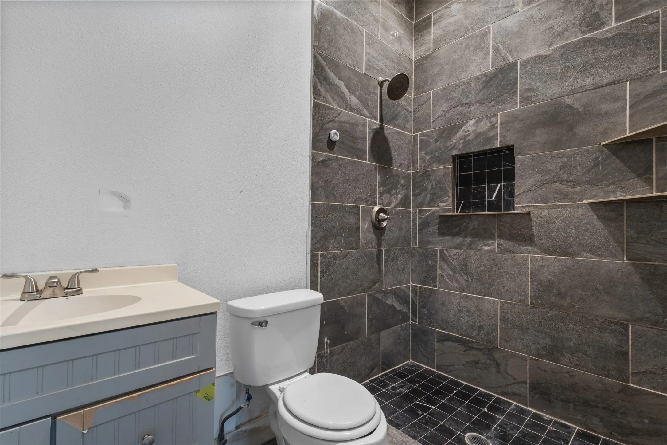 Shower with large format slate-style tile, built-in shelving, and a tiled niche