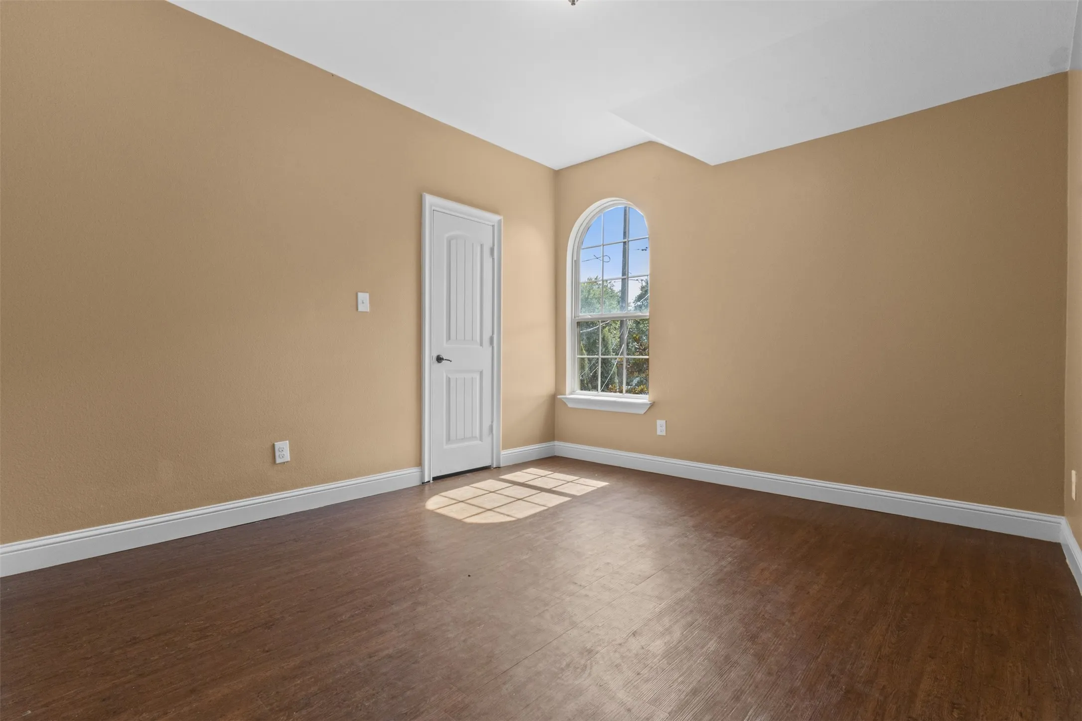 Arched window, wood-finish flooring, light tan walls, white trim, and a white paneled door