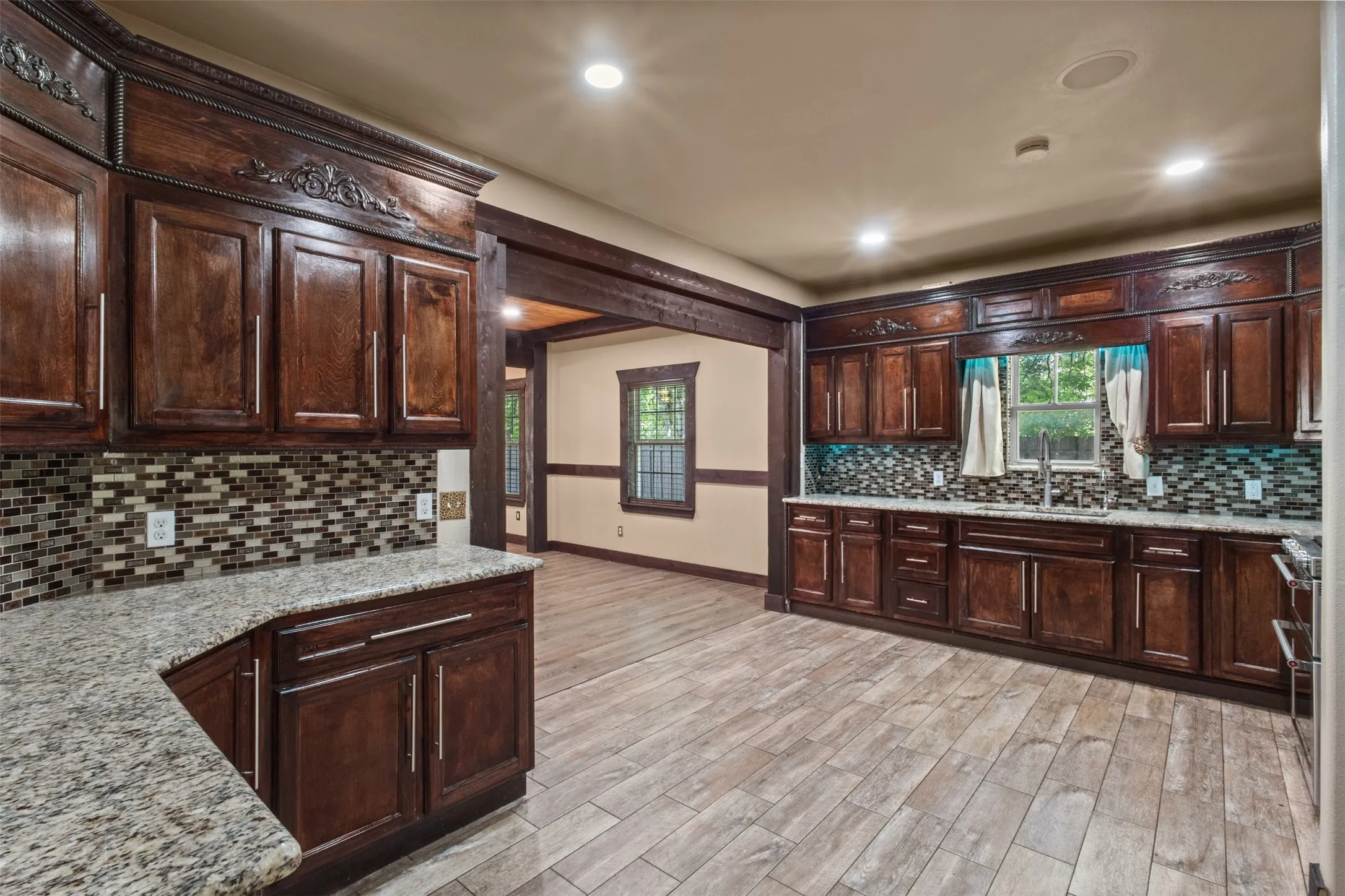 Kitchen featuring extensive dark wood cabinetry with ornate crown molding, light-toned granite countertops, and a mosaic tile backsplash