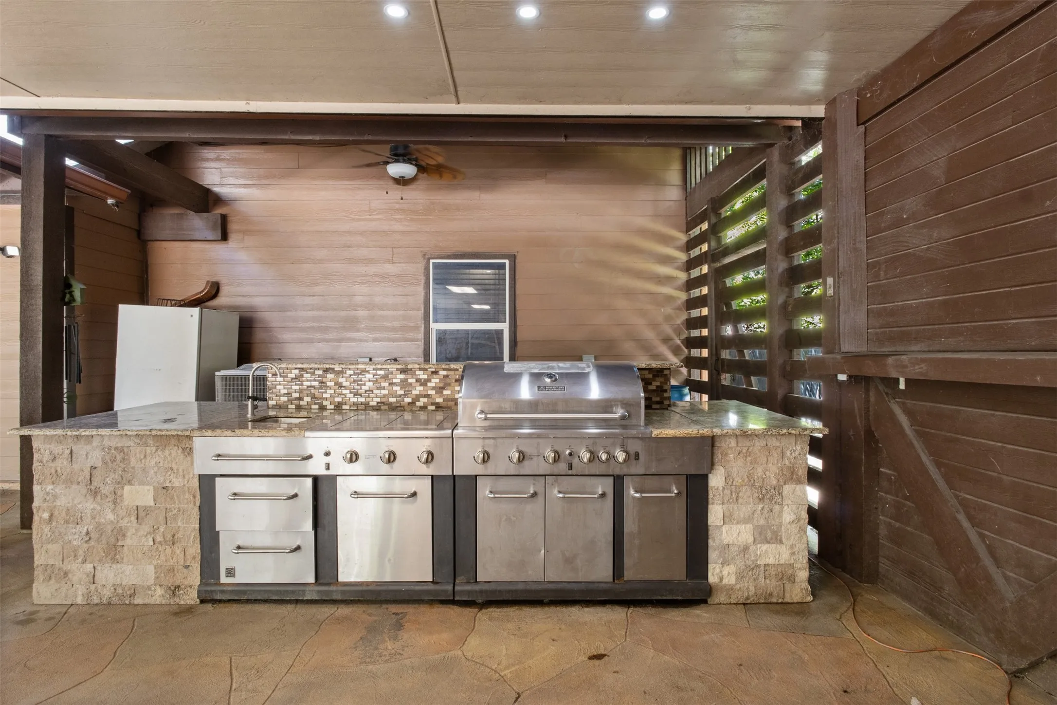 Outdoor kitchen featuring a built-in stainless steel grill, stone-clad island, and granite-look countertops
