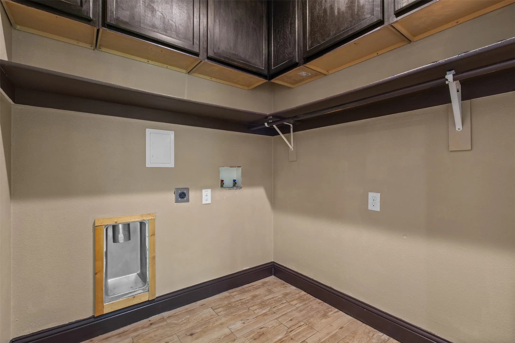 Dedicated utility space featuring wood-finish flooring, dark wood cabinetry, a dark wood shelf with white support brackets, and essential appliance hookups