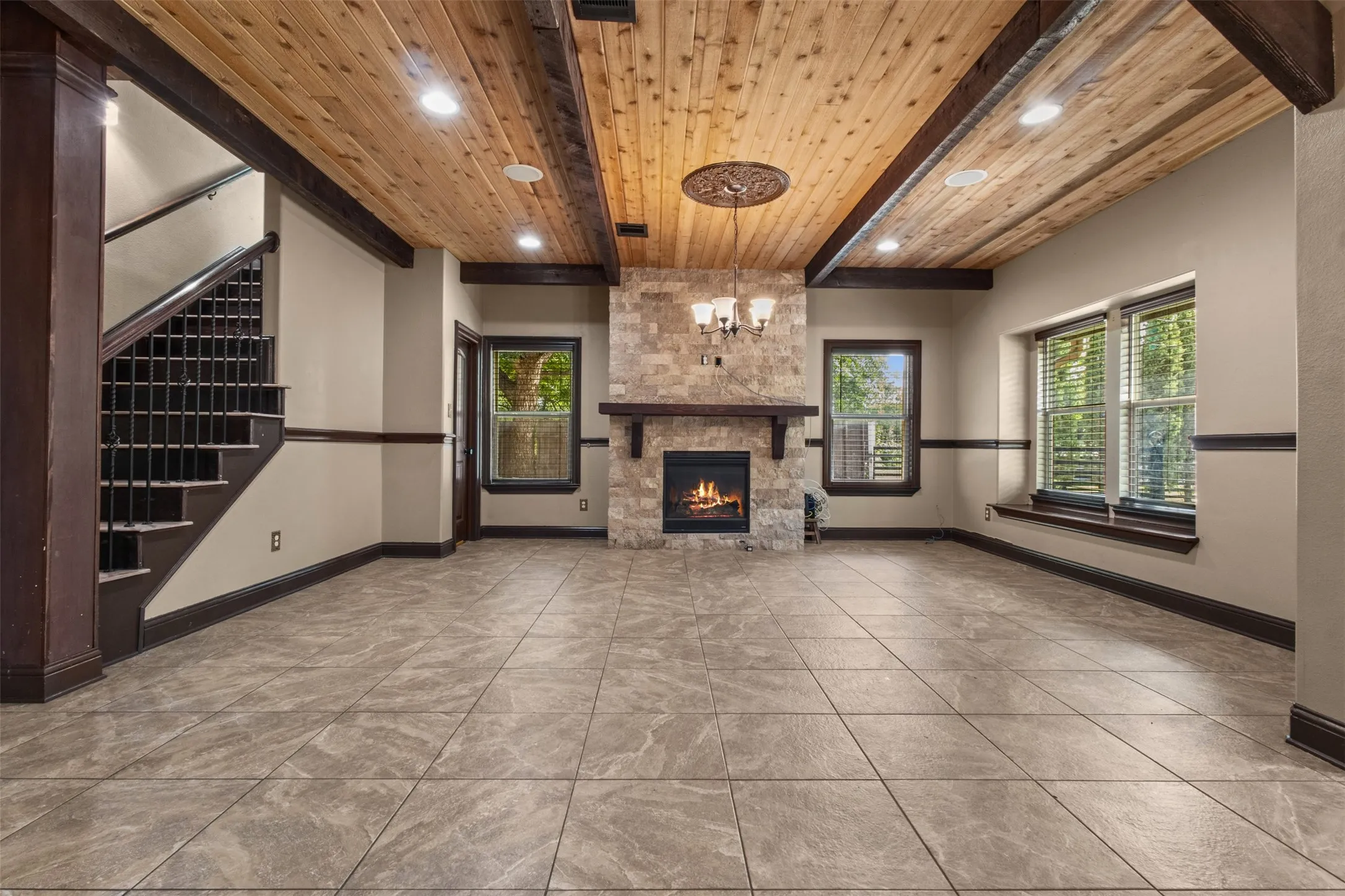 Spacious room featuring a stone fireplace with a wood mantle, a wood-paneled ceiling with exposed beams, recessed lighting, and large windows with blinds