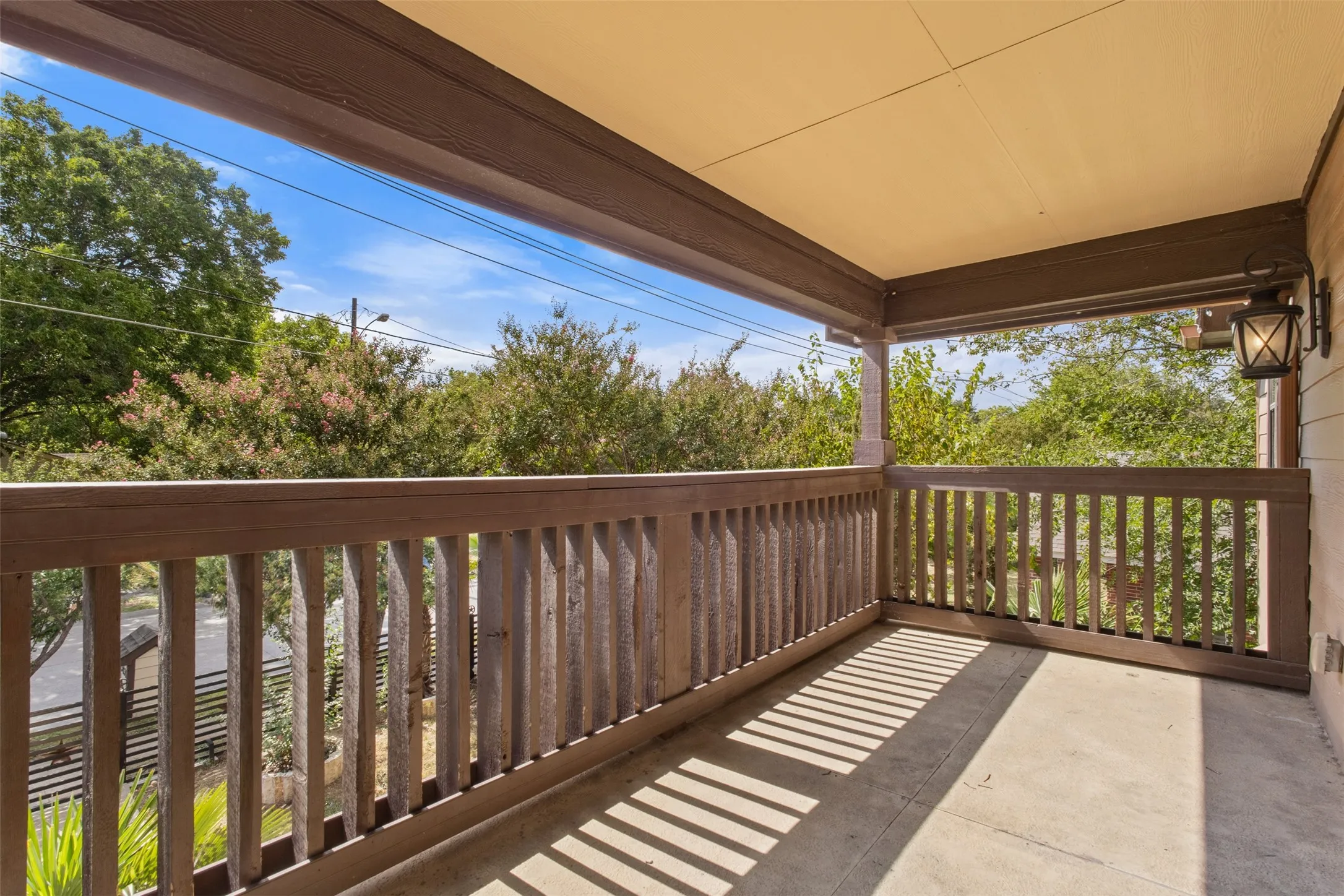 Covered balcony with concrete flooring, wood railing, and a wall-mounted lantern light fixture
