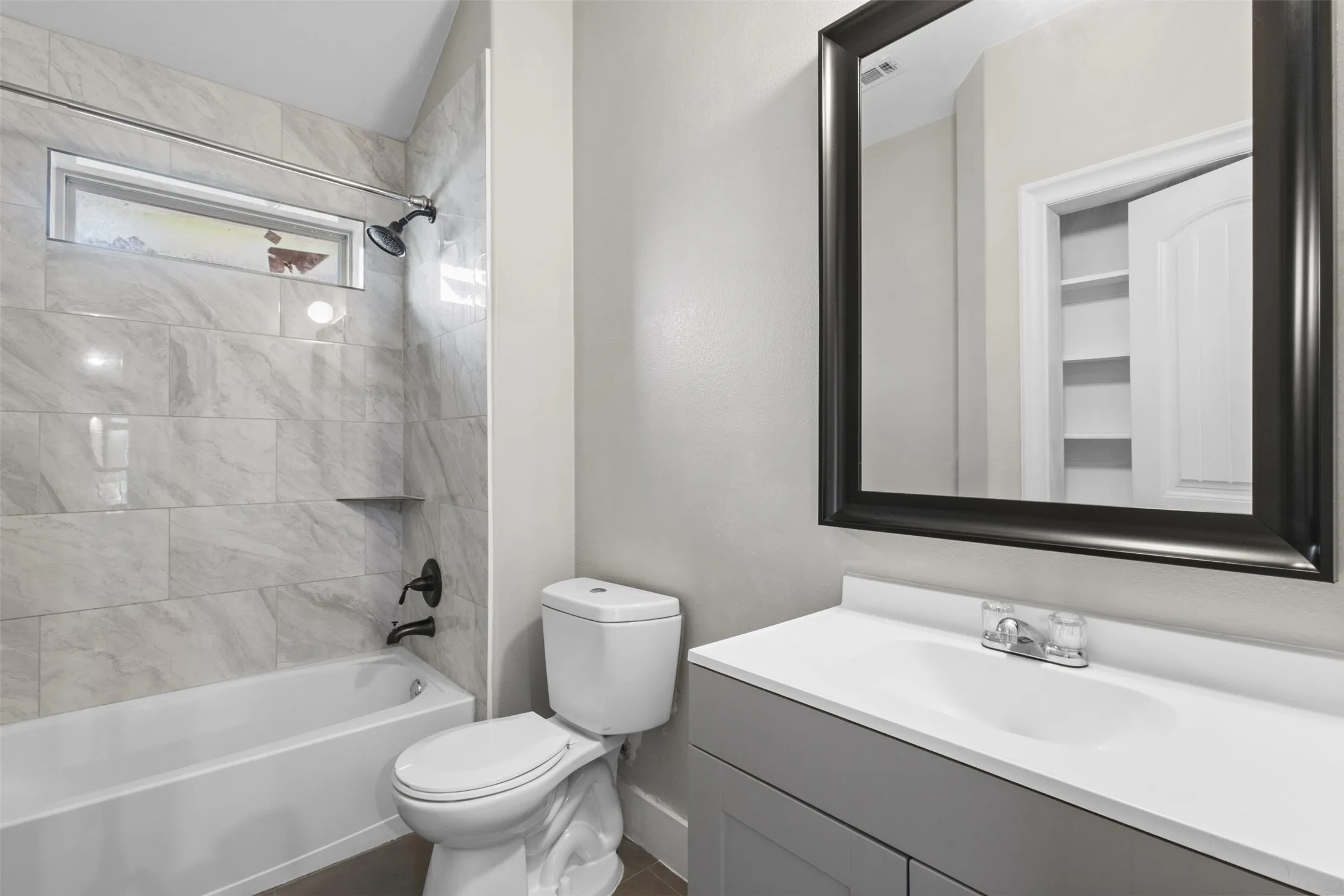 Bathroom featuring a white bathtub with a tiled surround, a built-in shower niche, and a horizontal window