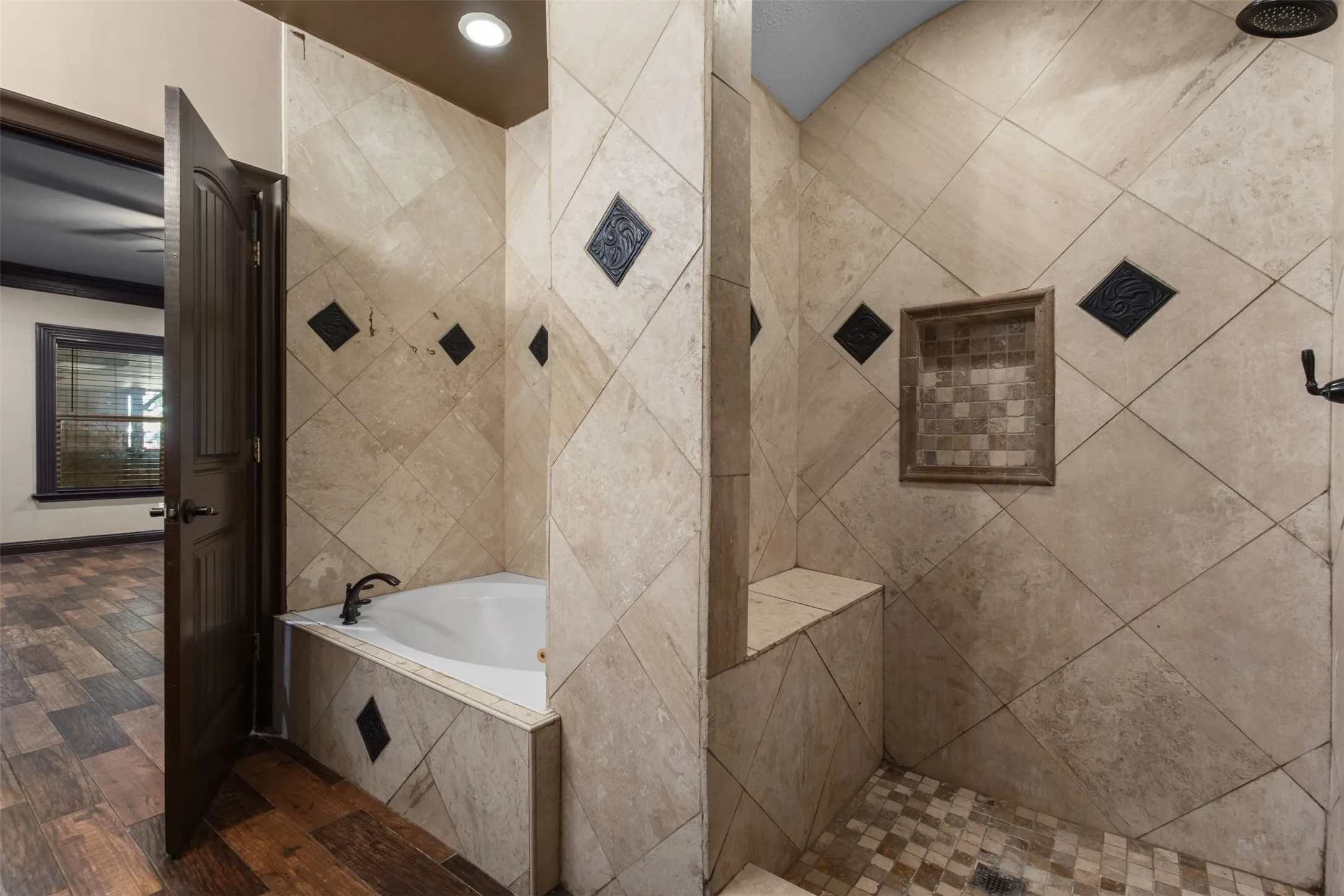 Tiled walk-in shower with a built-in bench and recessed niche, featuring a coordinating jetted tub with dark bronze fixtures