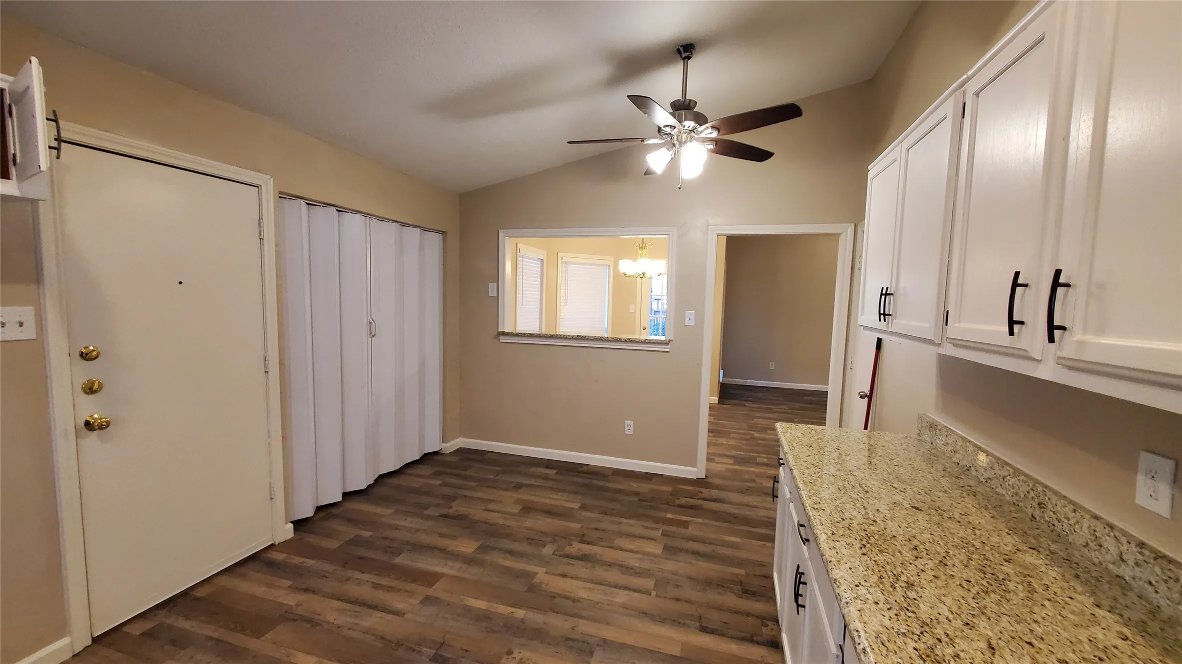 Kitchen with white cabinetry, light stone countertops, dark wood-type flooring, lofted ceiling, and ceiling fan with notable chandelier