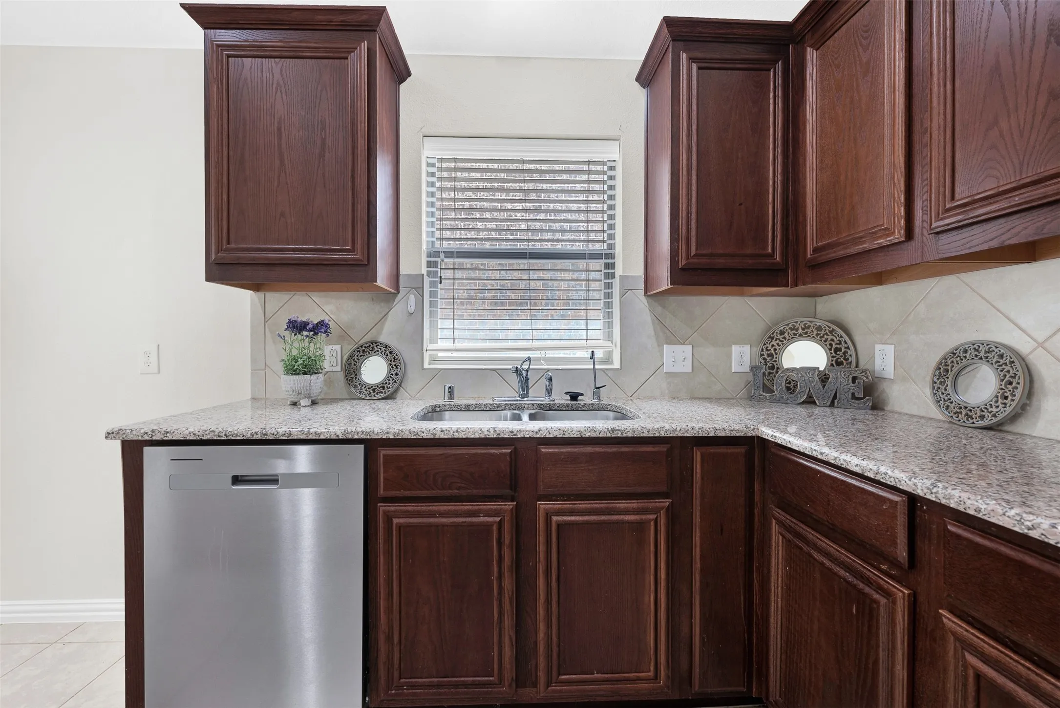 Kitchen featuring granite countertops, wood cabinetry, stainless steel dishwasher, and a tile backsplash