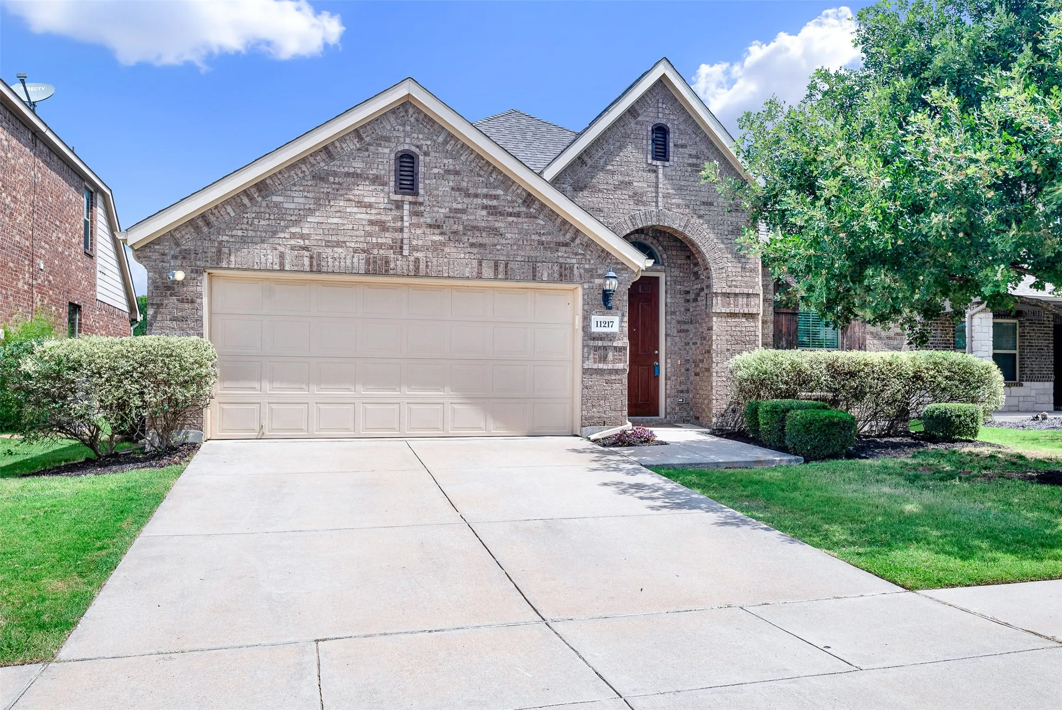 Brick facade residence featuring an arched entryway, gabled rooflines, an attached garage, and a concrete driveway