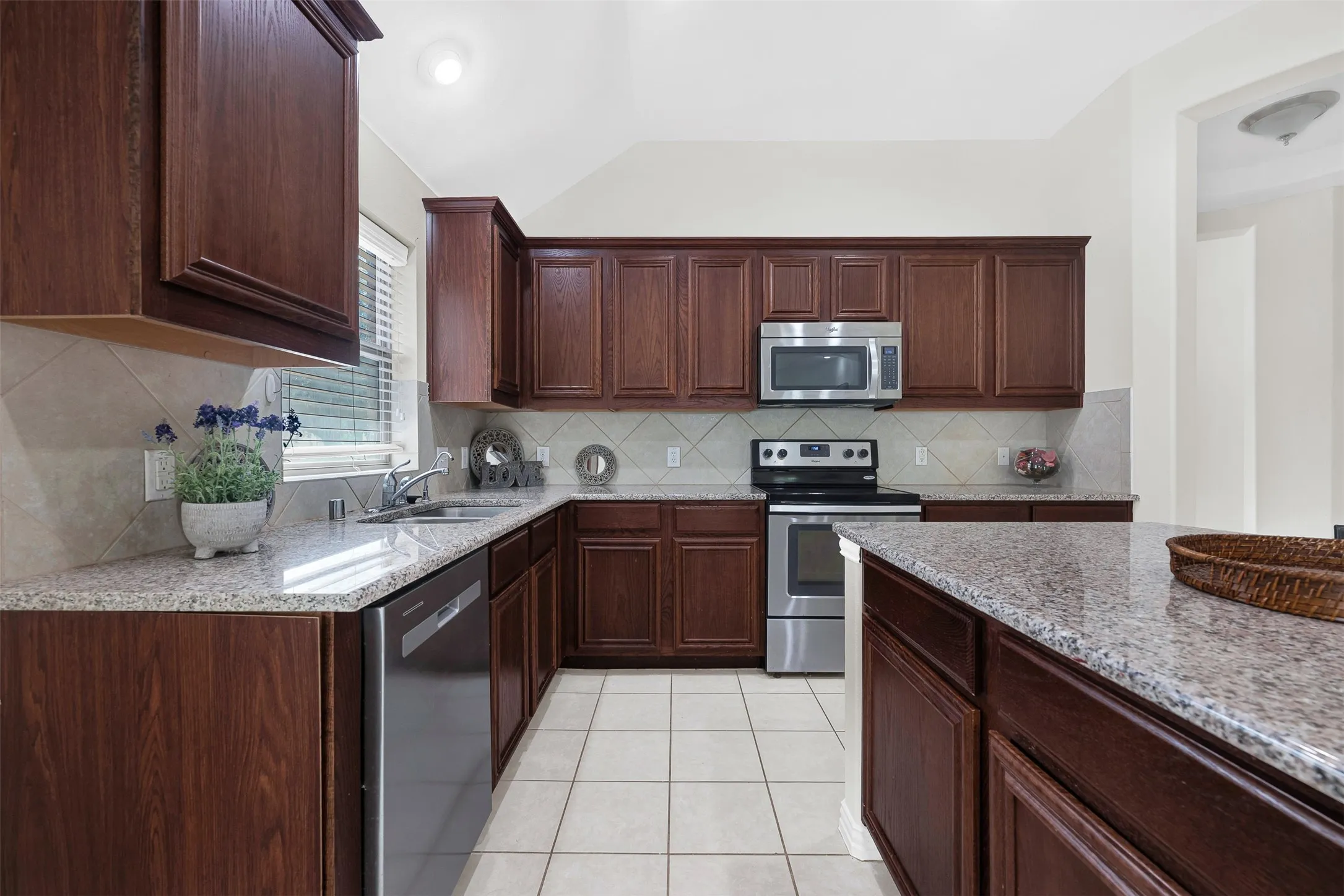 Kitchen featuring rich wood cabinetry, granite countertops, stainless steel appliances, a tile backsplash, and ceramic tile flooring