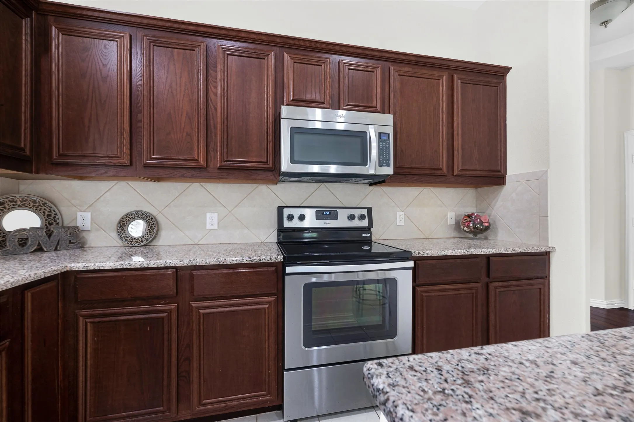 Kitchen featuring dark wood cabinetry, stainless steel oven and microwave, and light-toned granite countertops