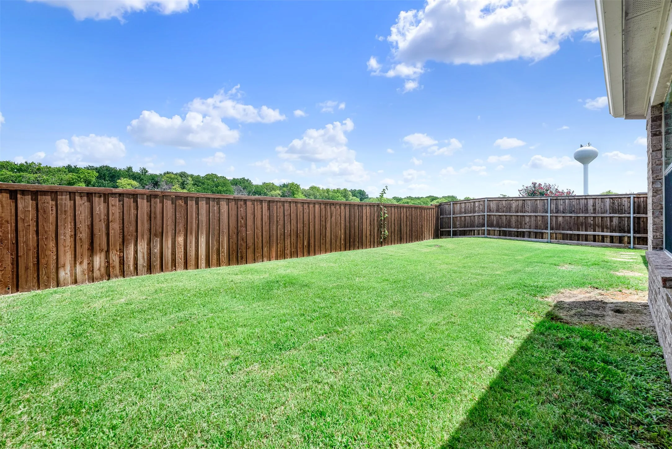 Spacious backyard featuring a manicured lawn, a full privacy fence, and a brick exterior wall