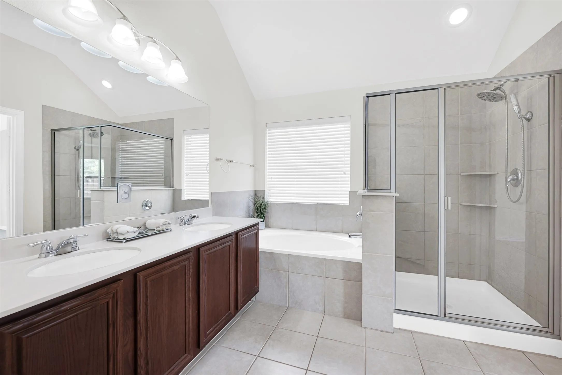 Bathroom featuring a dual vanity with dark wood-finish cabinetry, a large built-in mirror, an integrated soaking tub, and a glass-enclosed shower with tiled walls